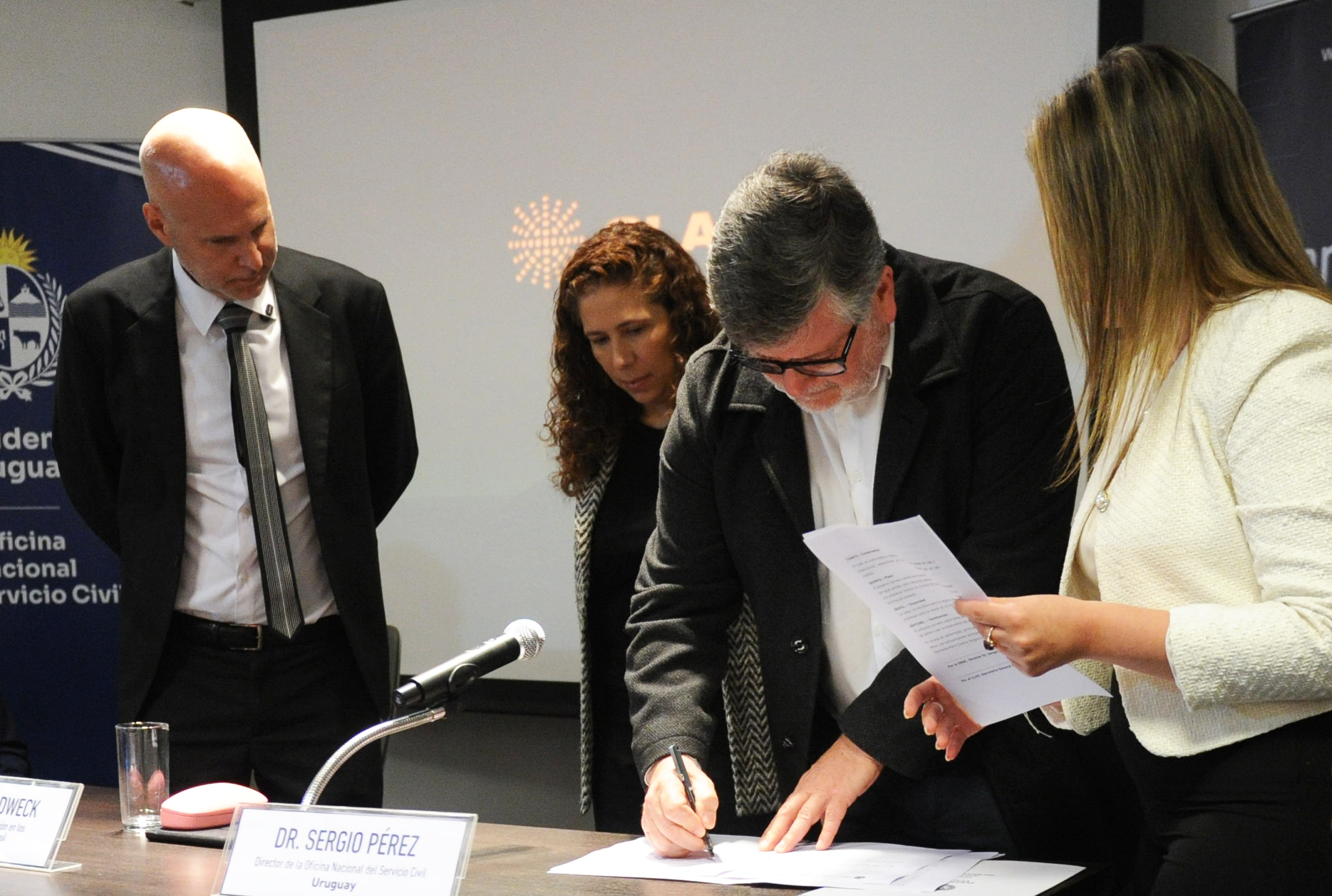 Director de la Oficina de Servicio Civil firma un documento mientras las demás autoridades lo observan.