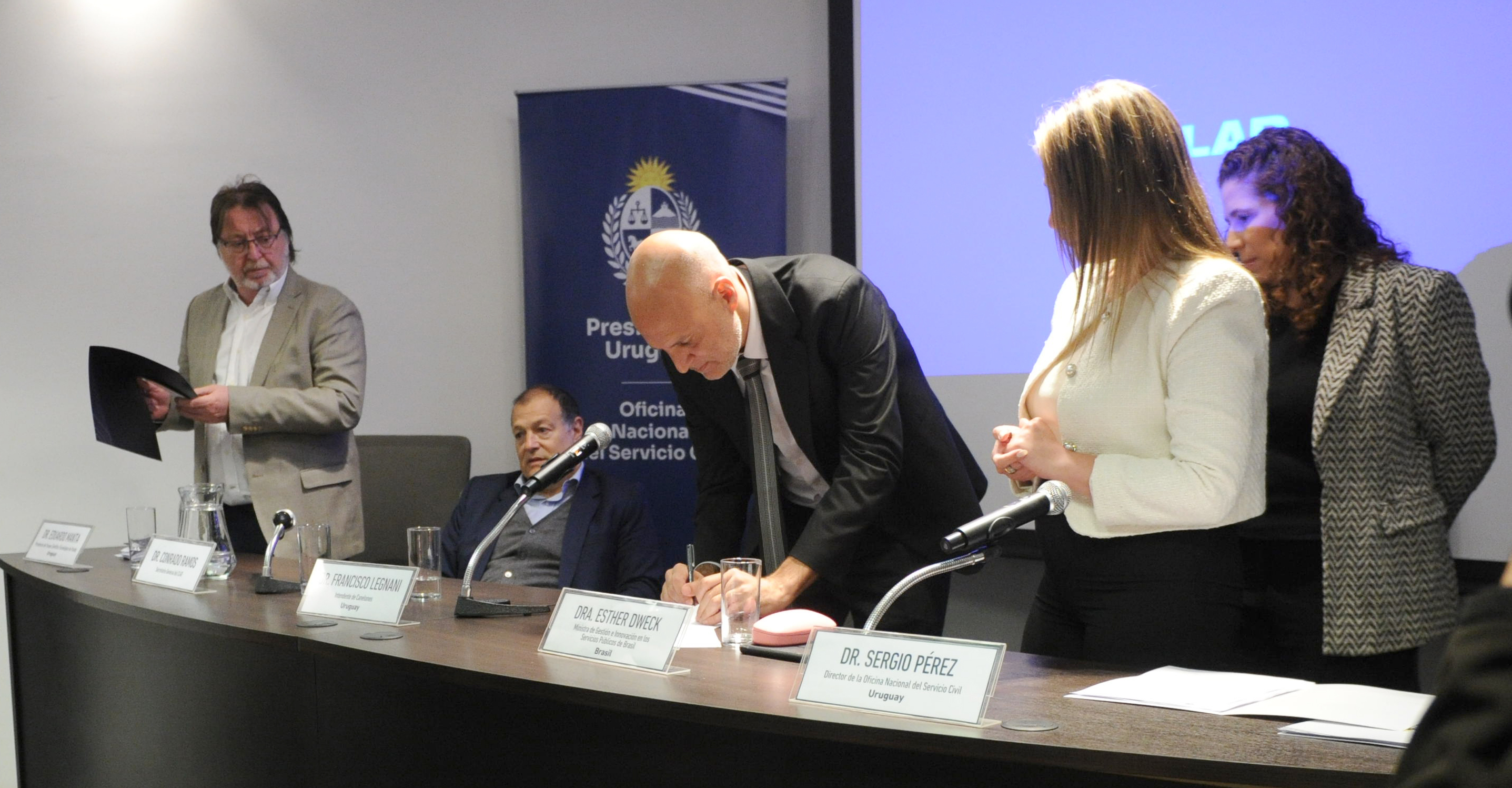 Intendente de Canelones firma un documento mientras las demás autoridades lo observan.