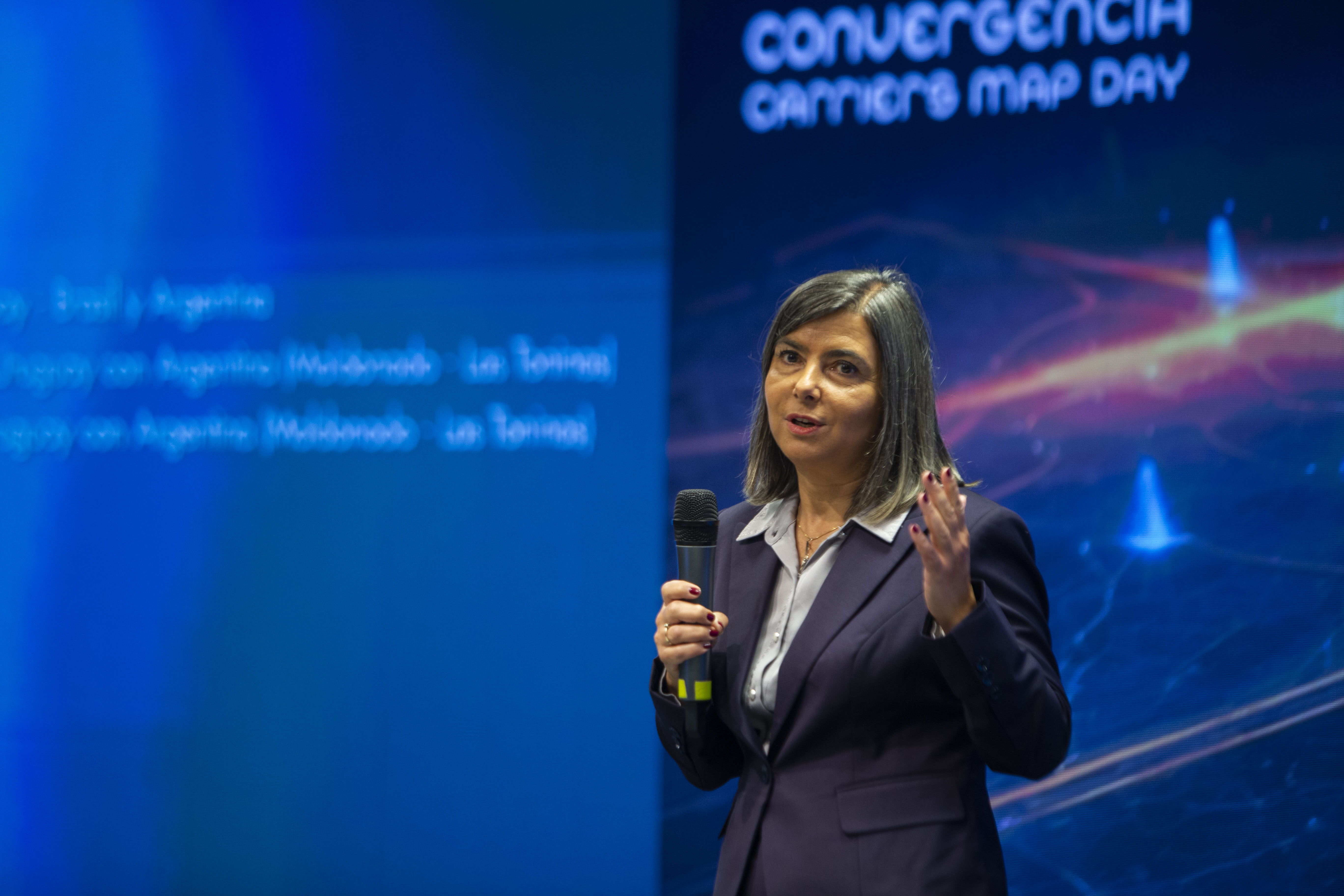 Gerenta general de Antel, de pie diserta con micrófono en mano en el escenario. Atrás se observa pantalla azul con la inscripción Convergencia.