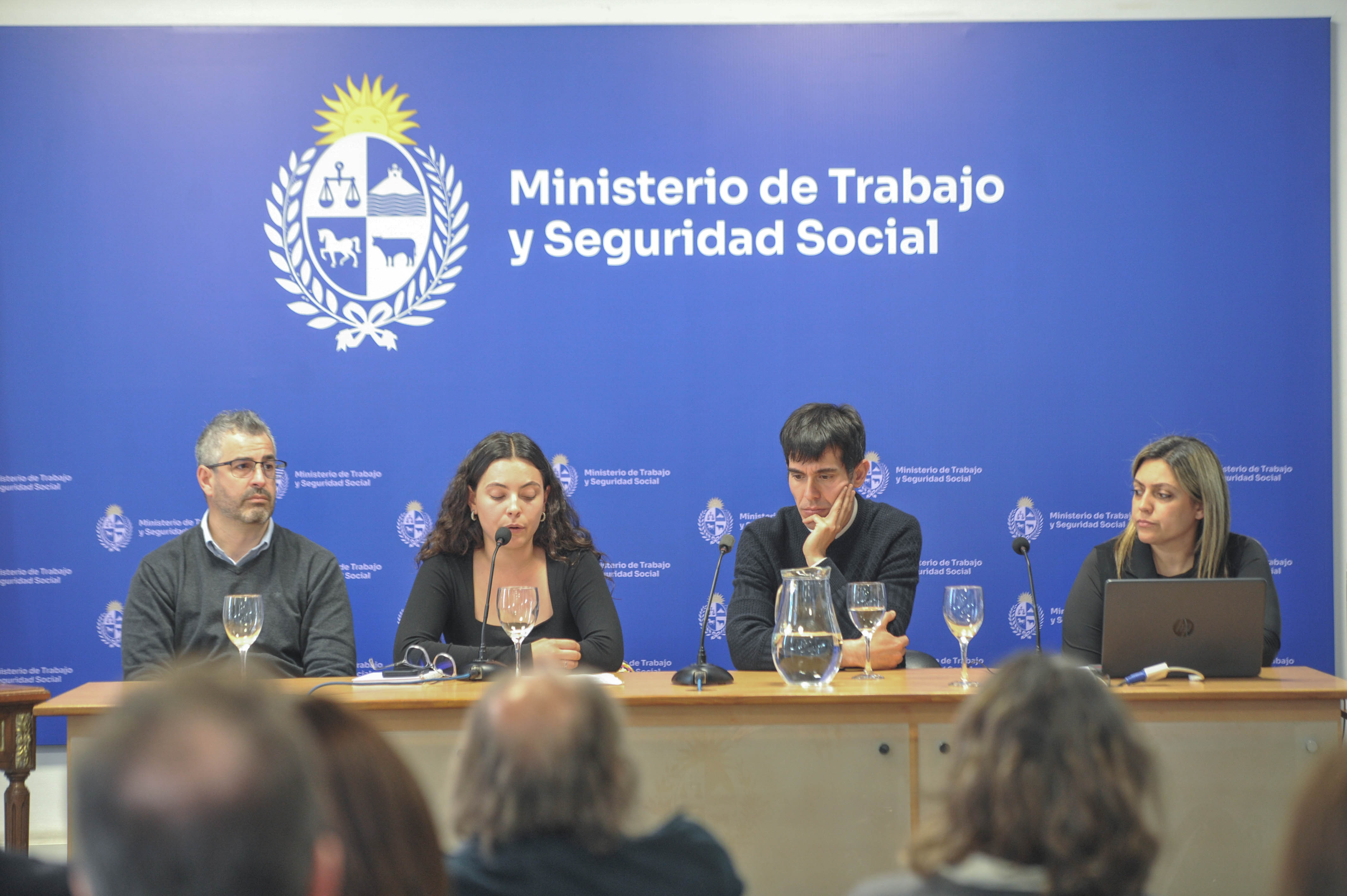 Directora del INJU diserta sentada en mesa principal con micrófono junto a autoridades del Ministerio de Trabajo.
