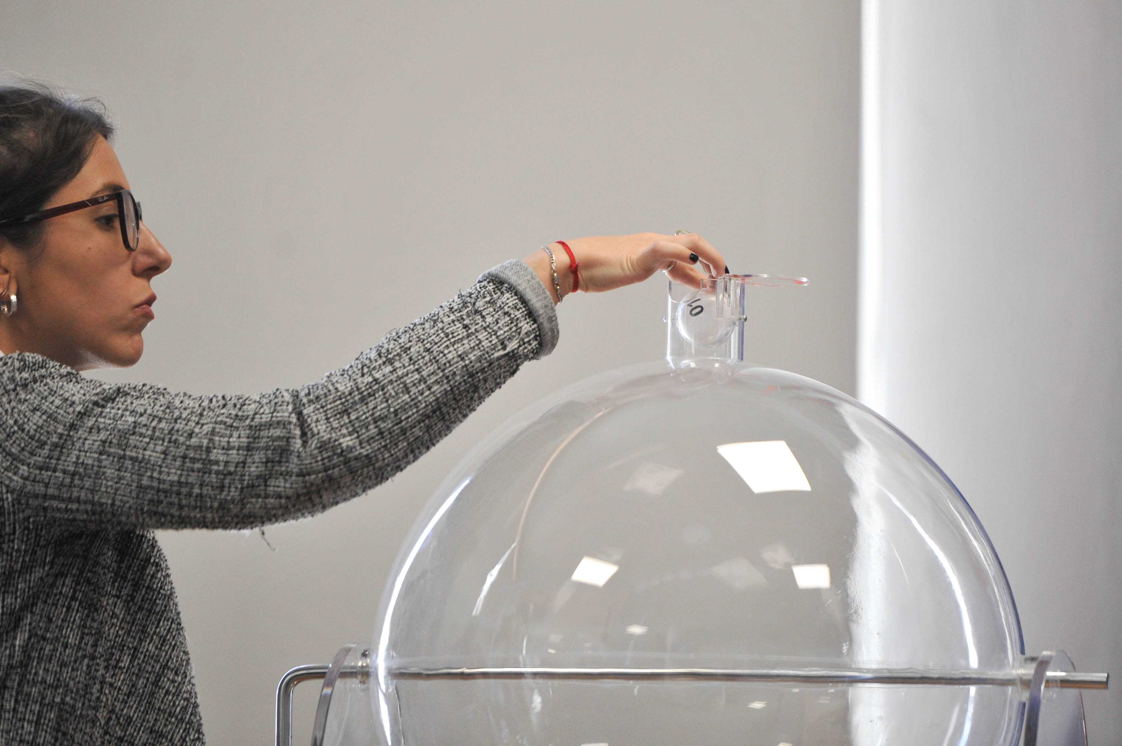 Primer plano de una mujer retirando una bola del bolillero transparente.