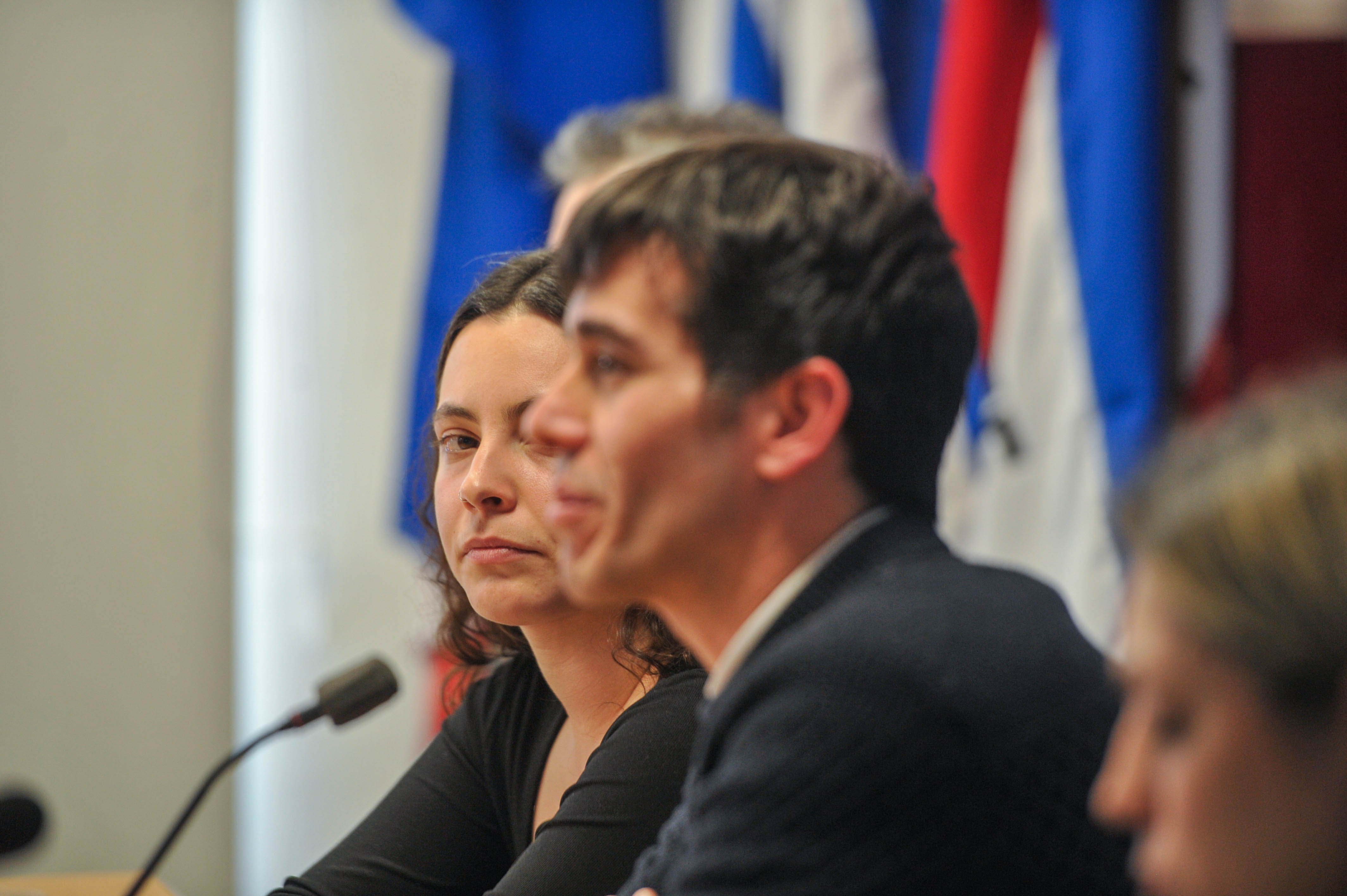 Director nacional de Trabajo, de perfil, diserta sentado en mesa con micrófono. A su costado, la directora del INJU lo observa.