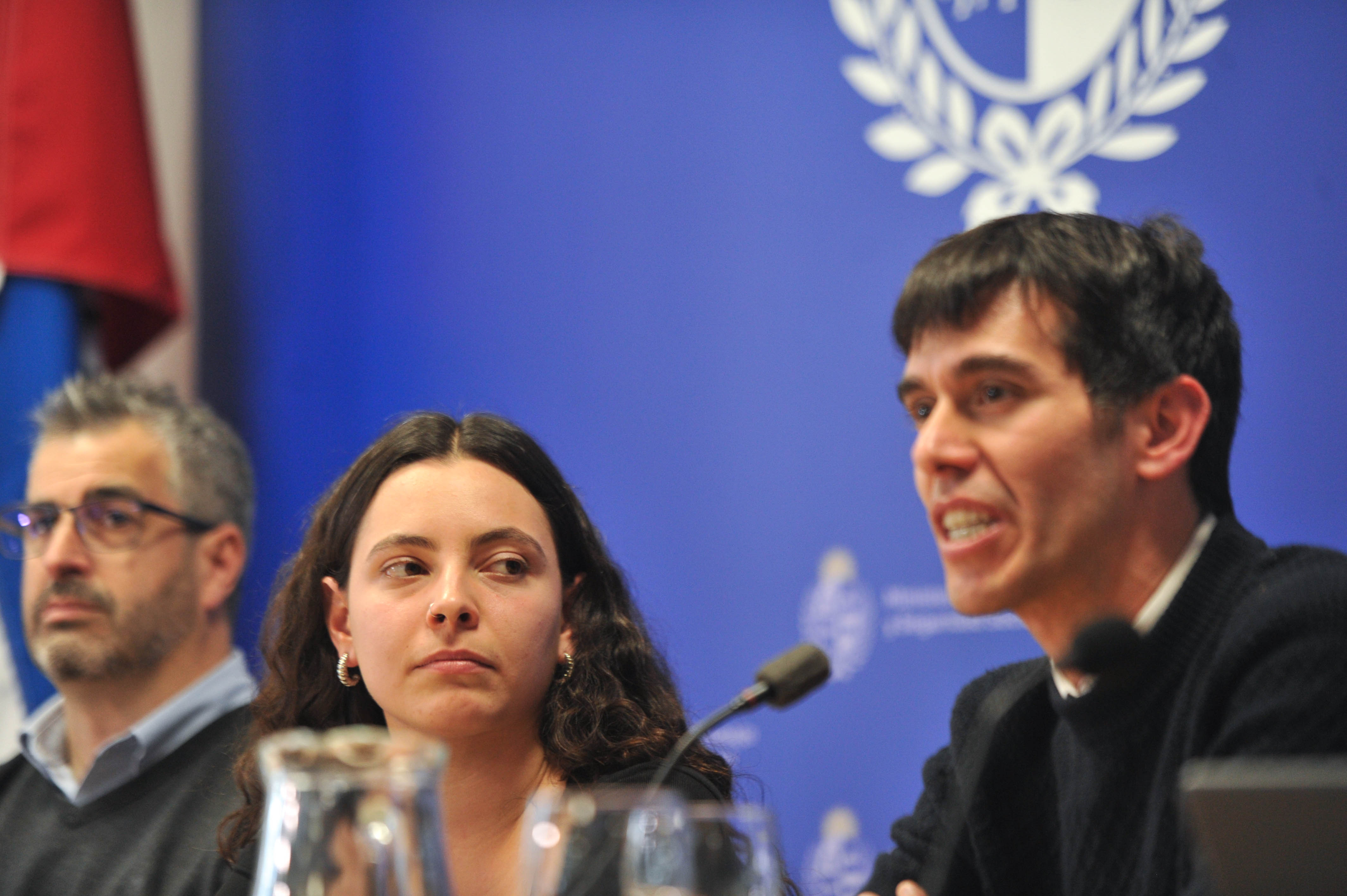 Primer plano del bolillero transparente con bolas alineadas en la bandeja de salida. Atrás se observa cartel azul con logo del ministerio.