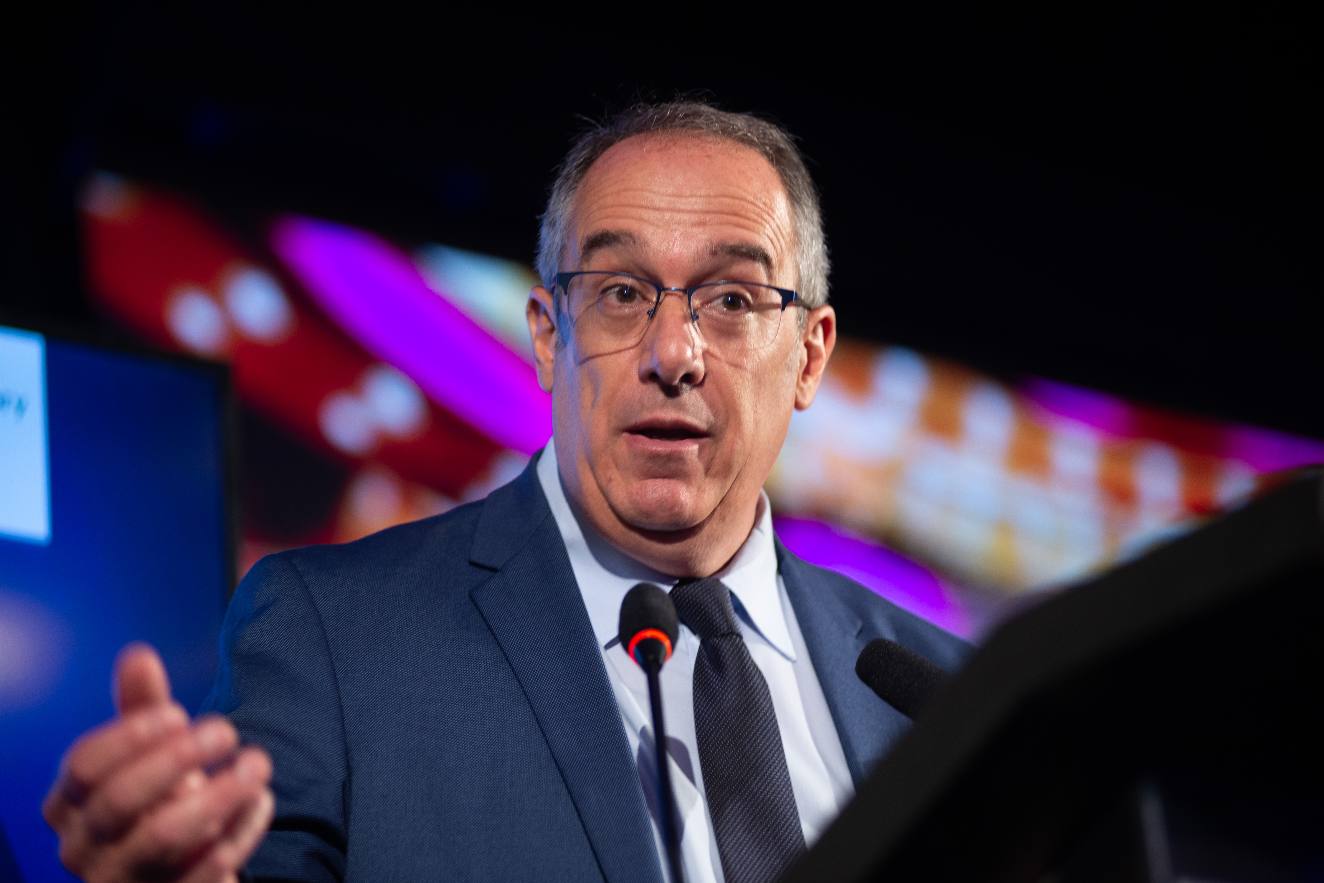 Ministro de Educación y Cultura diserta de pie en atril con micrófono en la sala de conferencia del hotel Radisson.