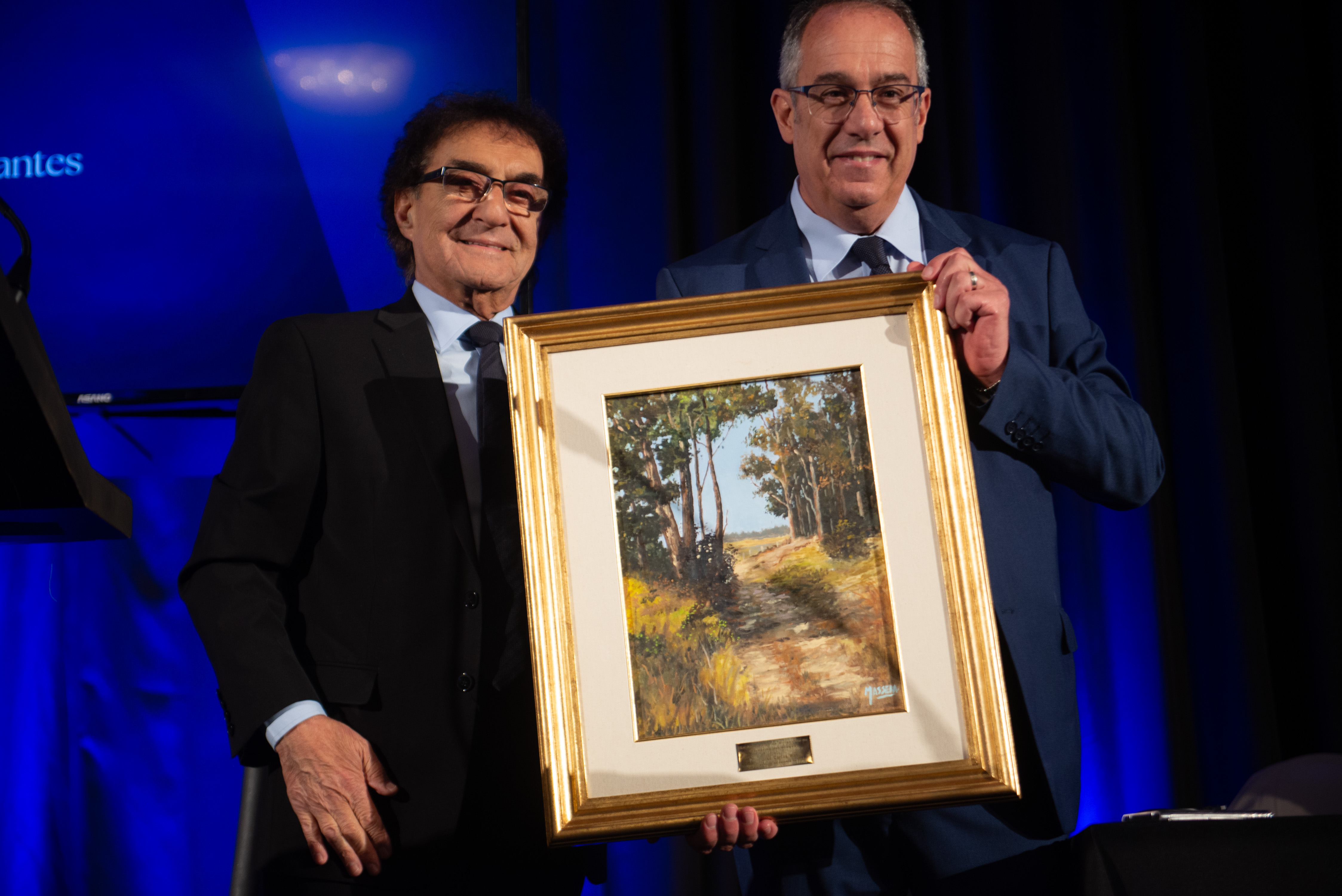 Ministro de Educación junto al presidente de ADM posa sonriente frente a cámara sosteniendo un cuadro que le obsequió la asociación.