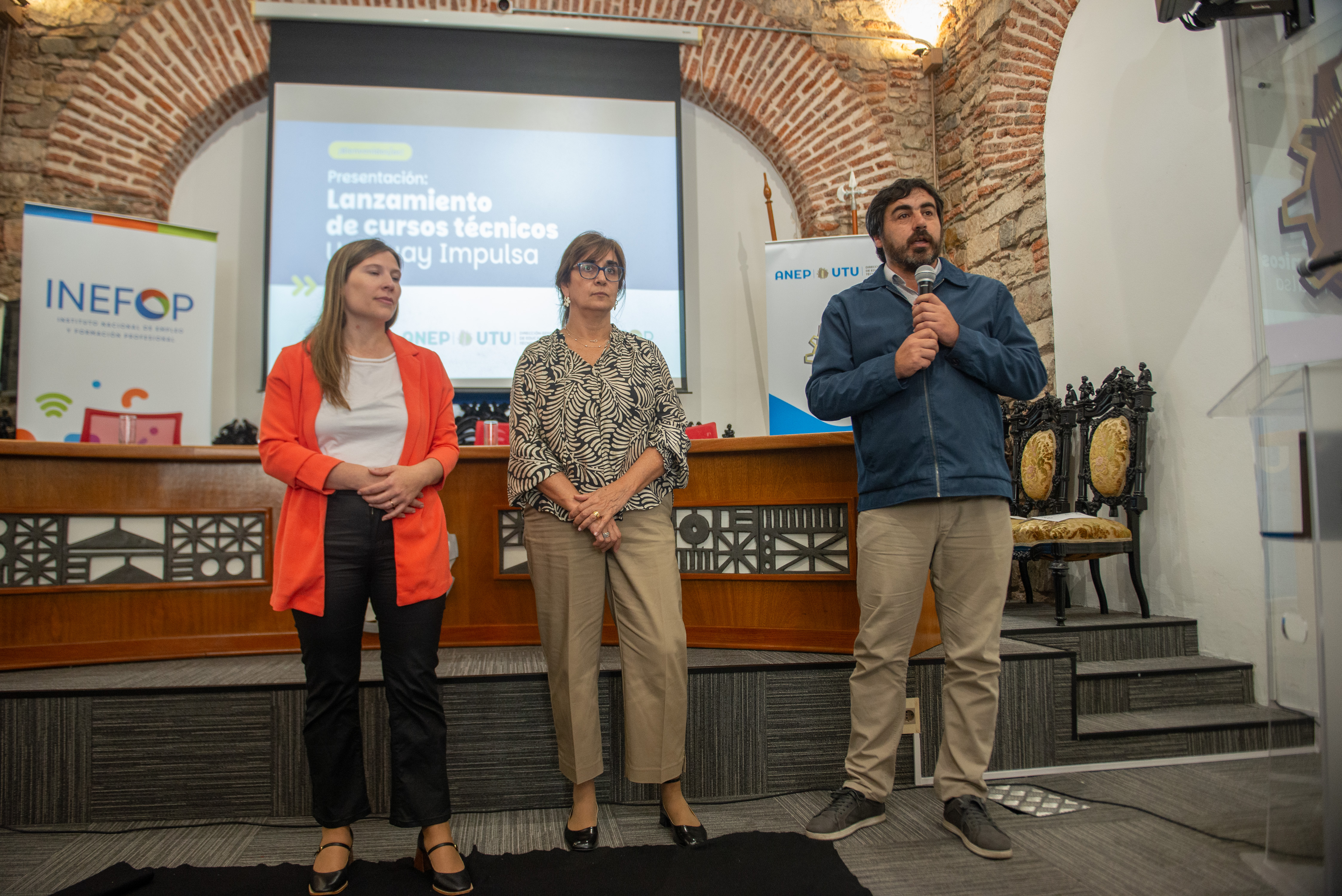 Director de Gestión Académica de UTU diserta, de pie, con micrófono en mano. A su costado hay dos técnicas de Inefop escuchando.