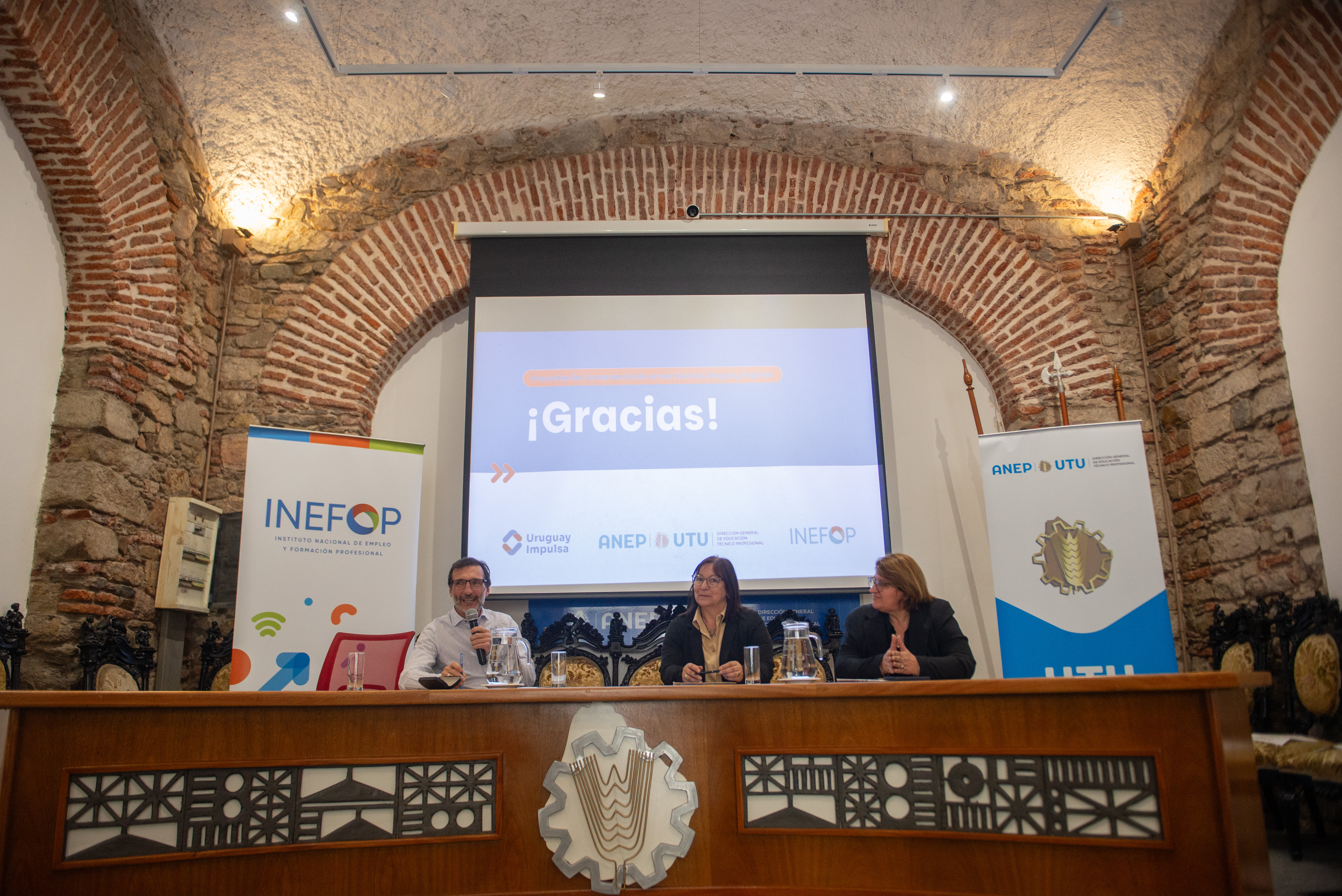 Directores de Inefop y UTU y consejera de la ANEP sentados en mesa con micrófonos. Atrás proyección final de "¡Gracias!" y logos de UTU e Inefop.