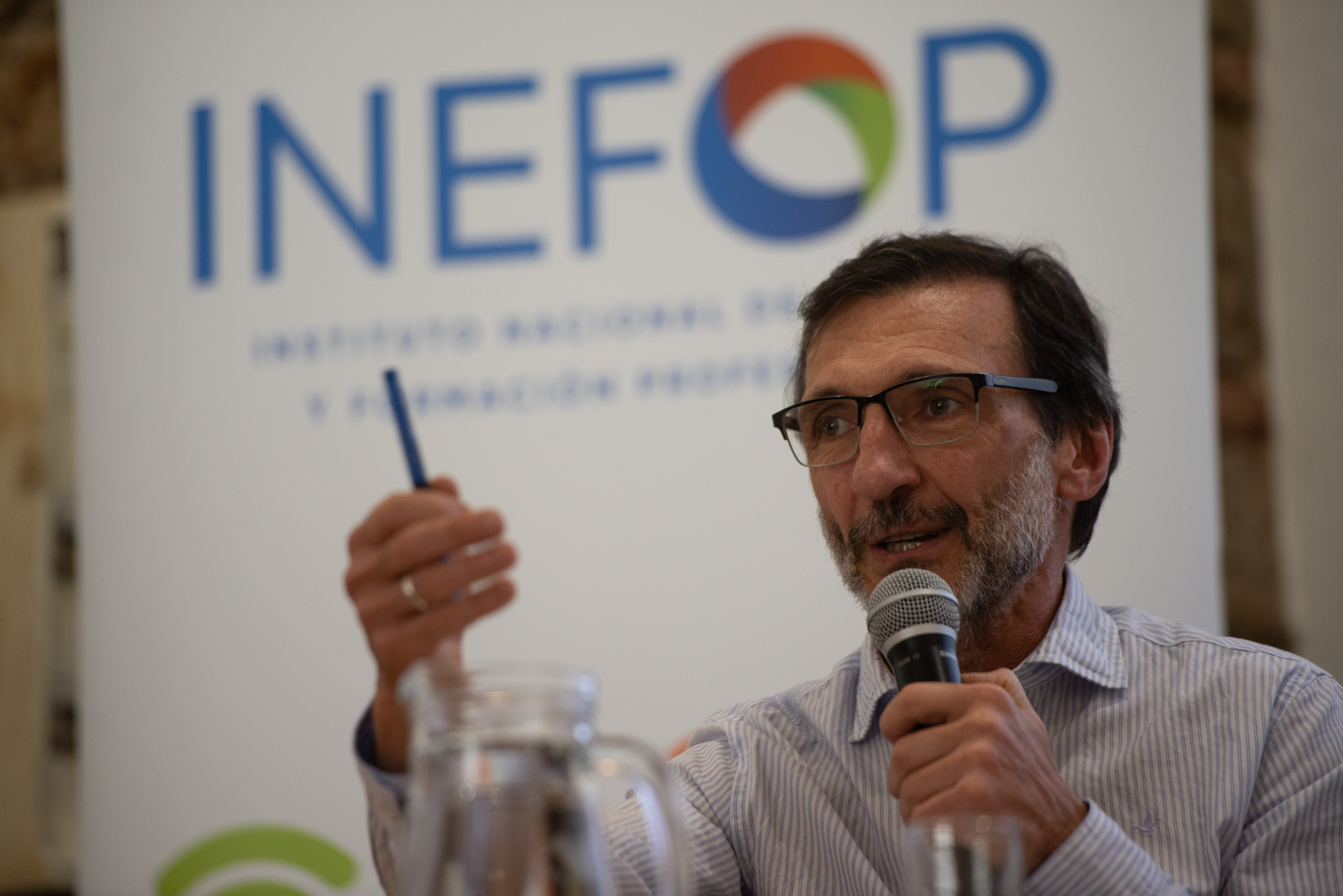 Director general de Inefop diserta, sentado en mesa con micrófono, señalando con una lapicera. Detrás, cartel blanco con logo de Inefop.
