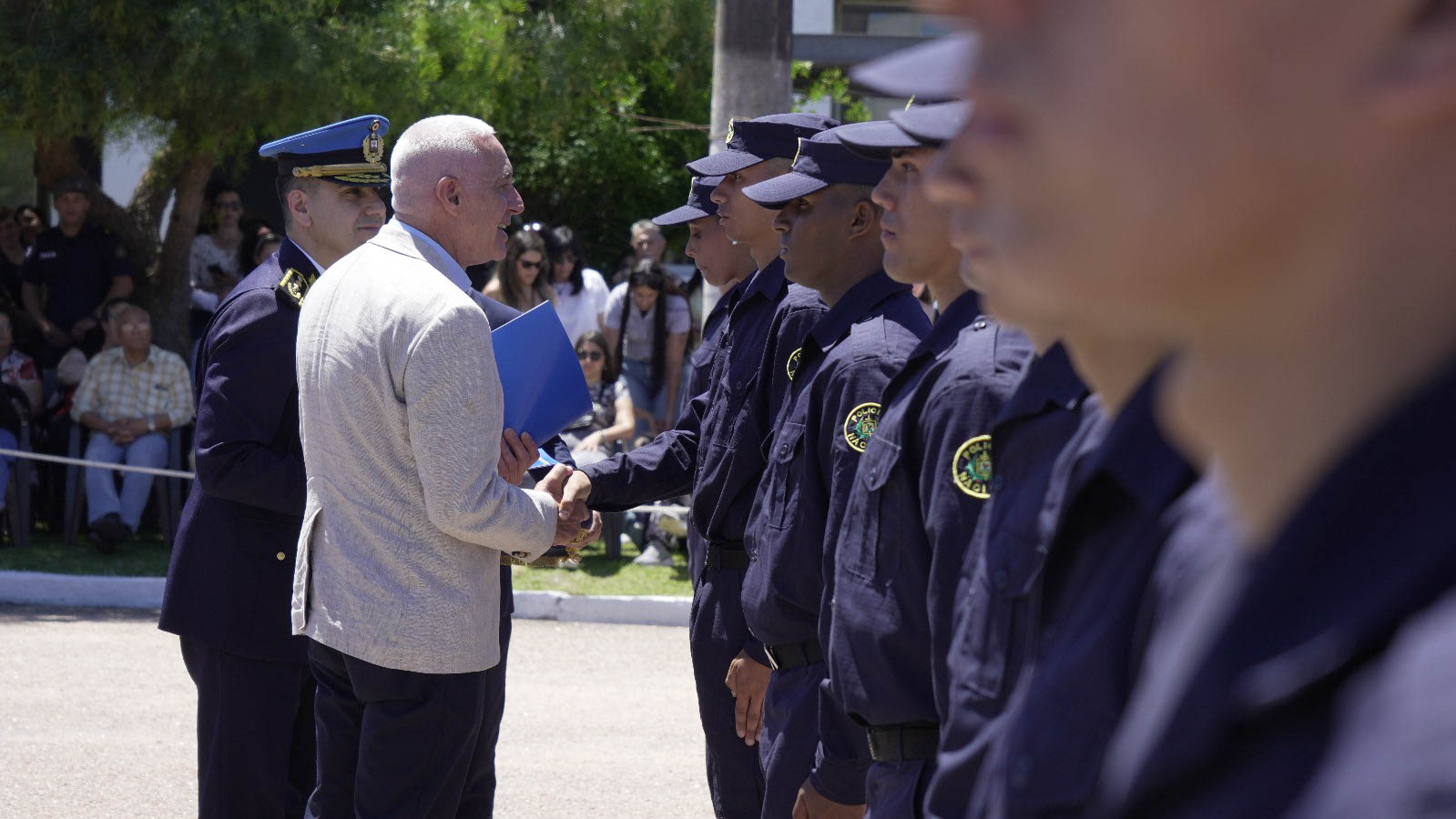 Ministro del Interior estrecha la mano de un policía en fila, mientras un oficial uniformado observa en la ceremonia egreso de efectivos policiales.