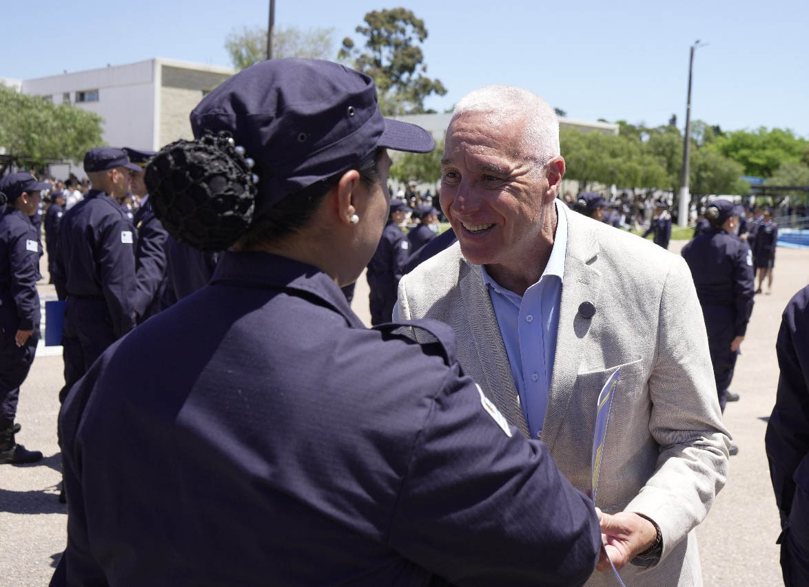 Ministro del Interior estrecha la mano de una oficial de policía que está de espaldas. Atrás se observan varios agentes formados.