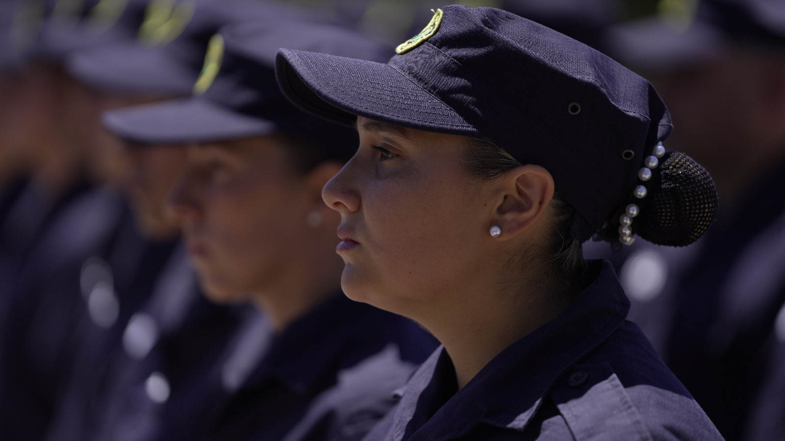 Primer plano de una mujer policía uniformada y en perfil. Permanece seria y atenta en la formación militar.