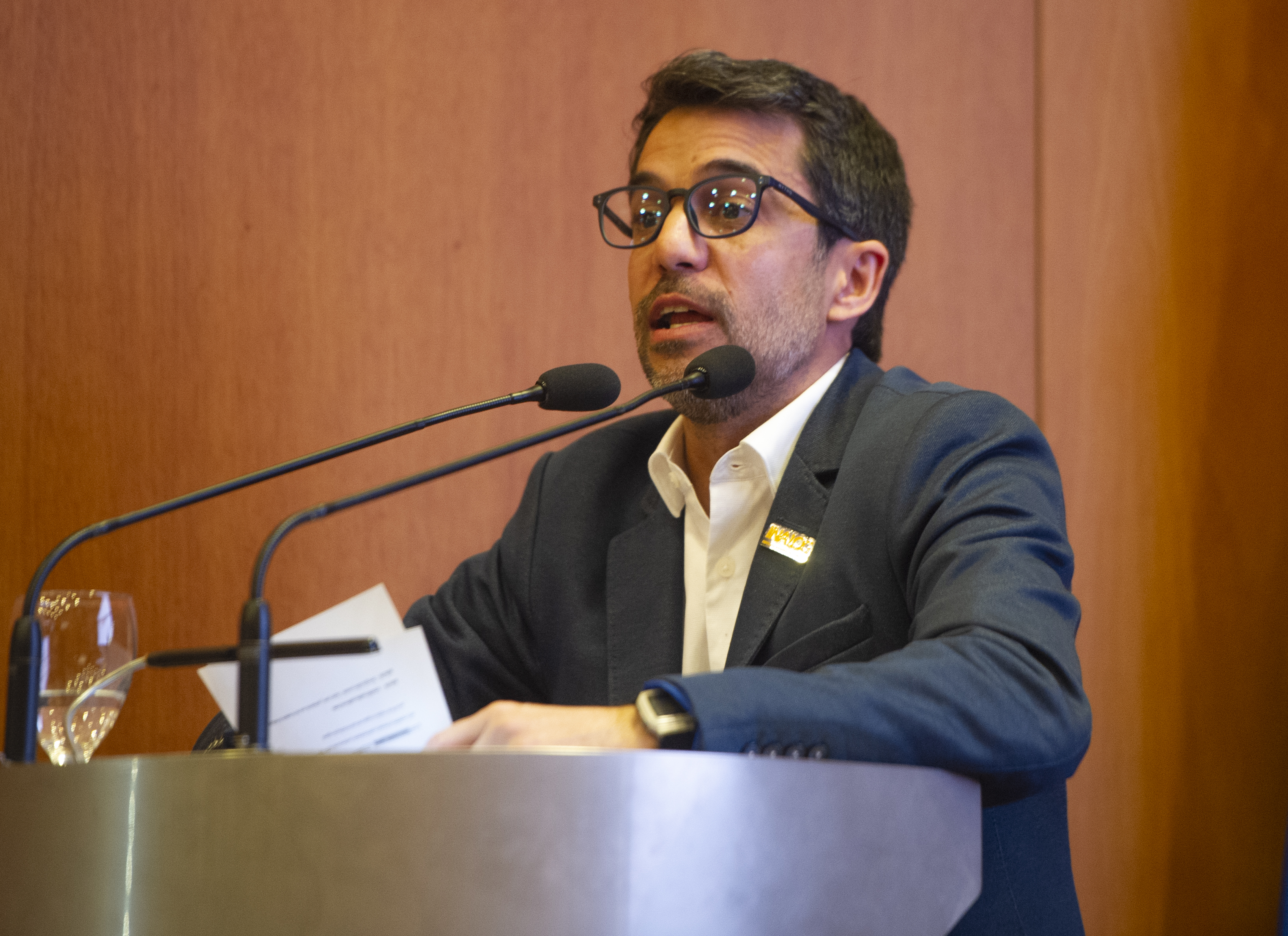 El presidente del Instituto Nacional de Logística, de pie, diserta en atril con micrófono en el escenario del auditorio de Presidencia.