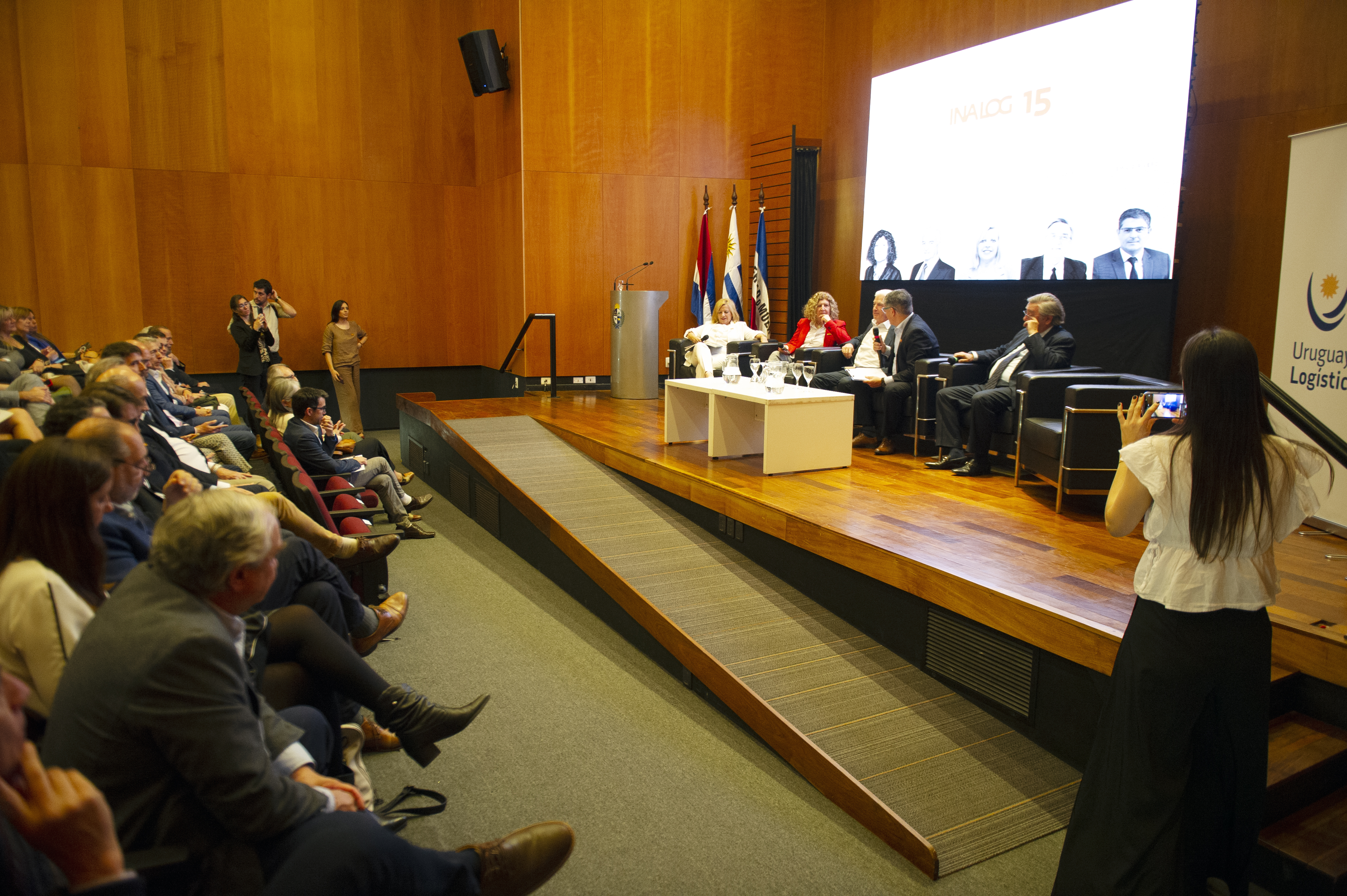 Público sentado en la platea mirando hacia el escenario donde cinco autoridades, sentadas en sillones, disertan.