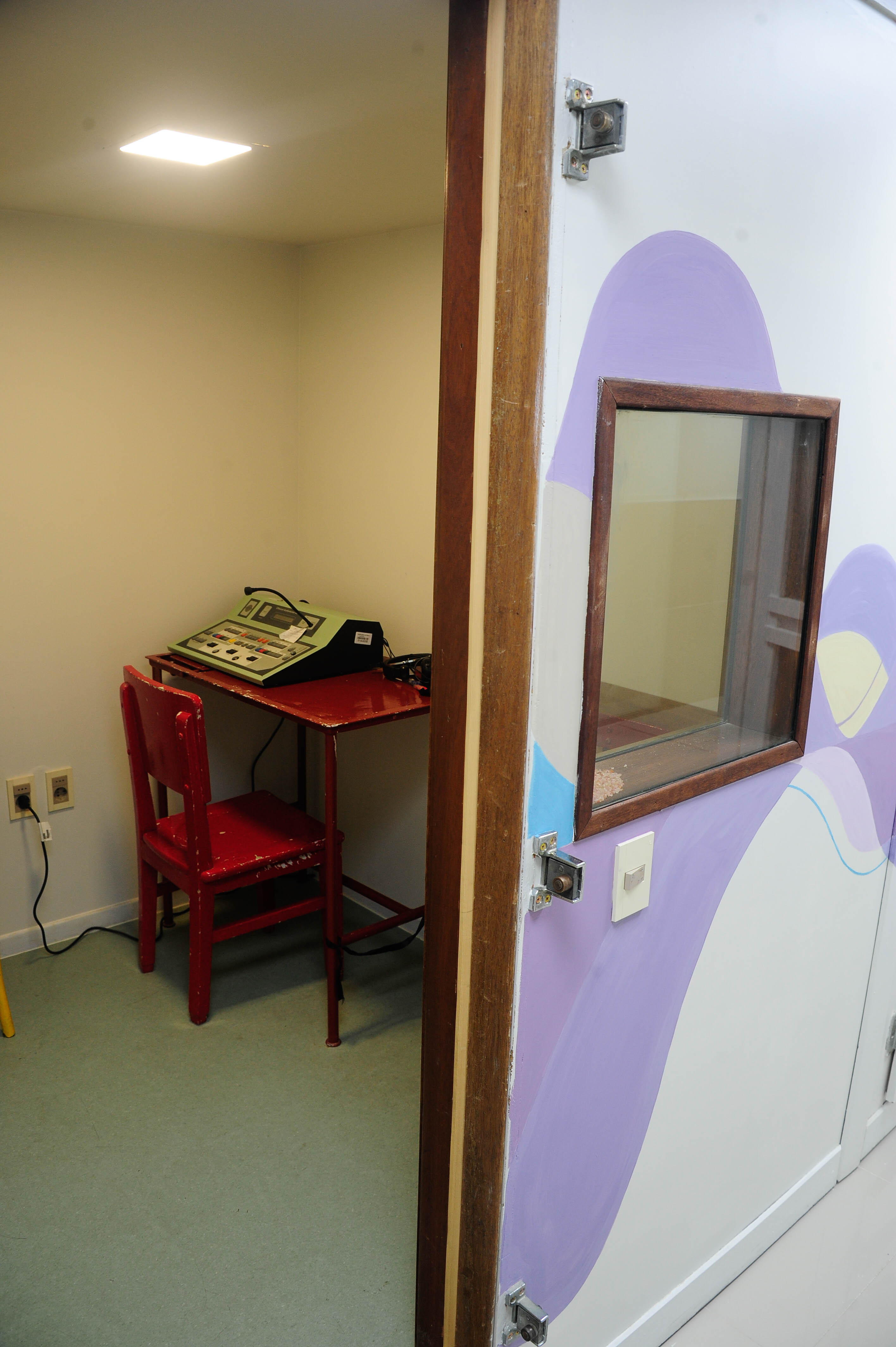 Foto de la entrada de la cabina para estudios de fonoaudiología donde se ve un equipo para esta especialidad sobre mesa roja.