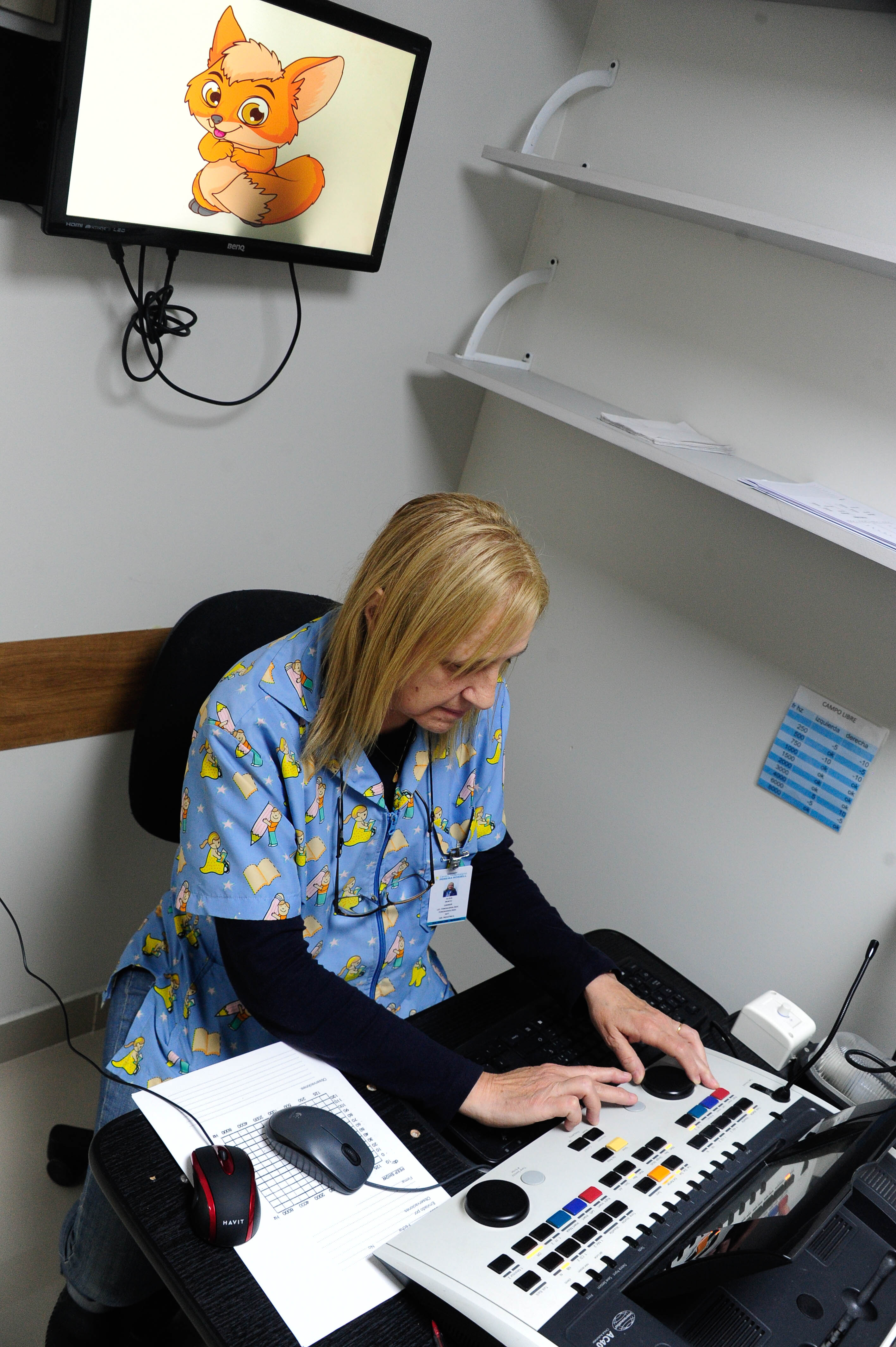 Plano general de una sala donde hay una técnica sentada en un escritorio operando un equipo especializado.