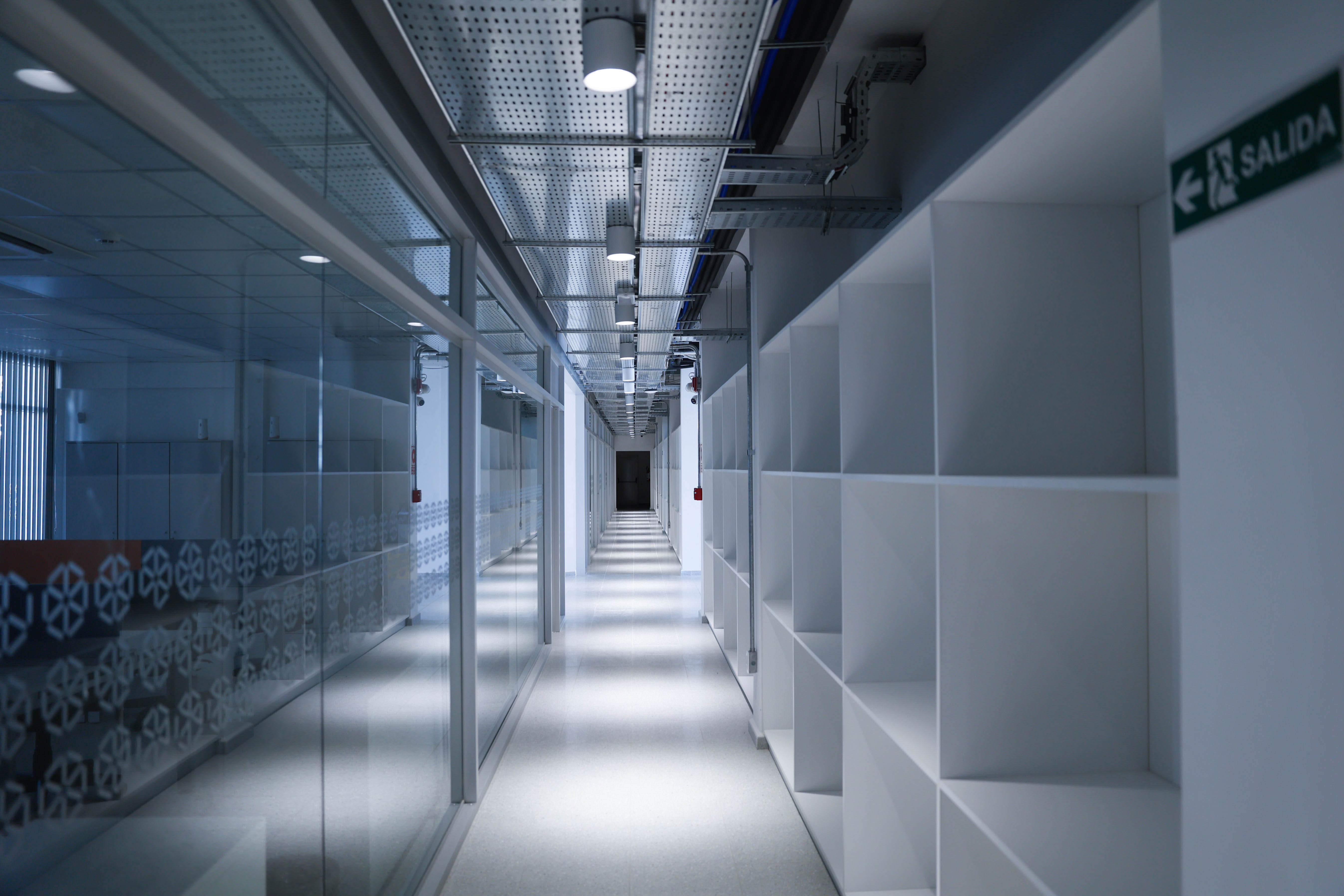 Pasillo interior moderno con paredes de vidrio y estantes blancos del nuevo edificio del Instituto Tecnológico Regional en Lavalleja.