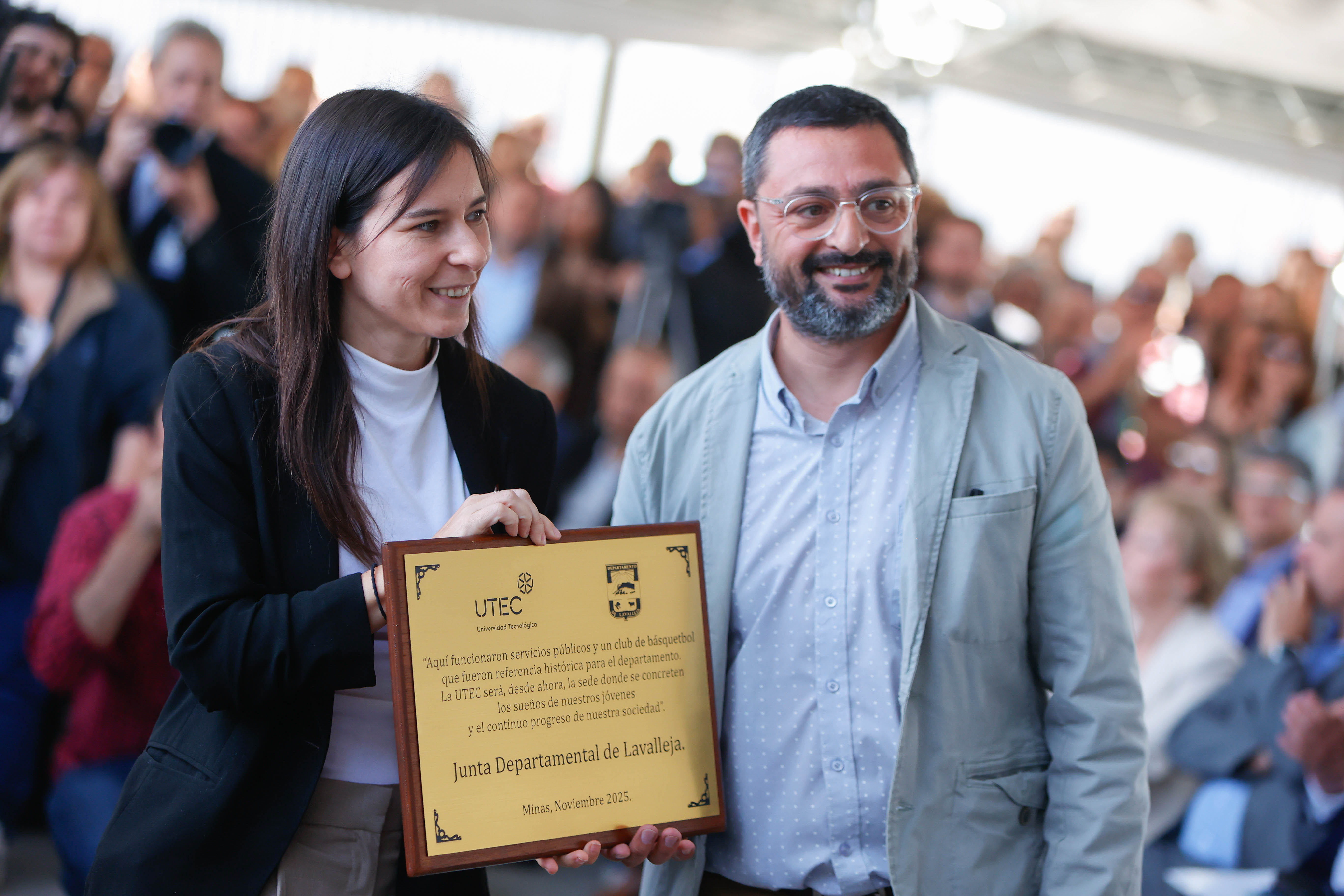 Rectora de UTEC posa sonriente frente a cámara junto a un hombre sosteniendo una placa dorada que le obsequió la Junta Departamental.