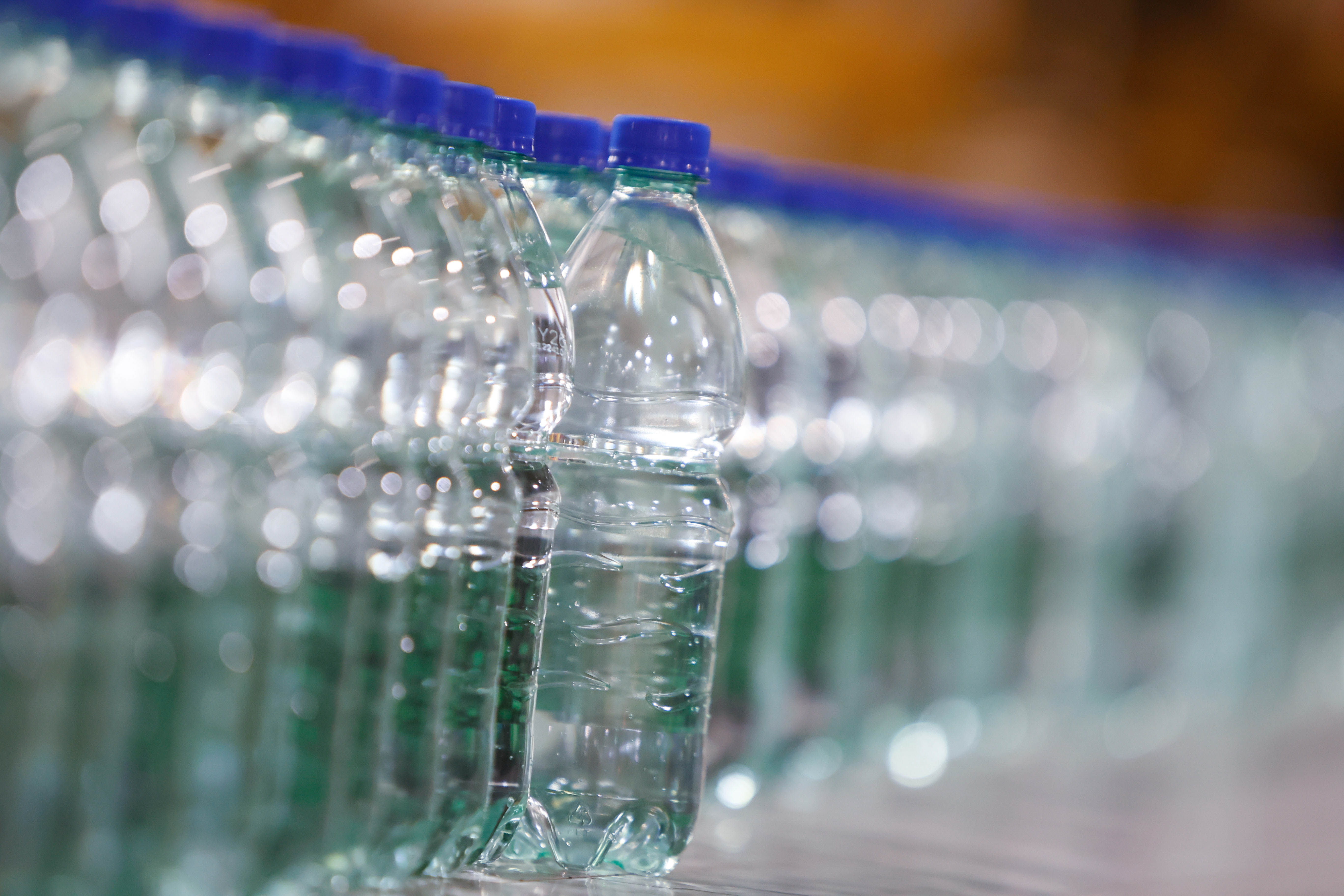 Primer plano de una hilera de botellas de plástico transparente con tapas azules, transportándose en una línea de producción.