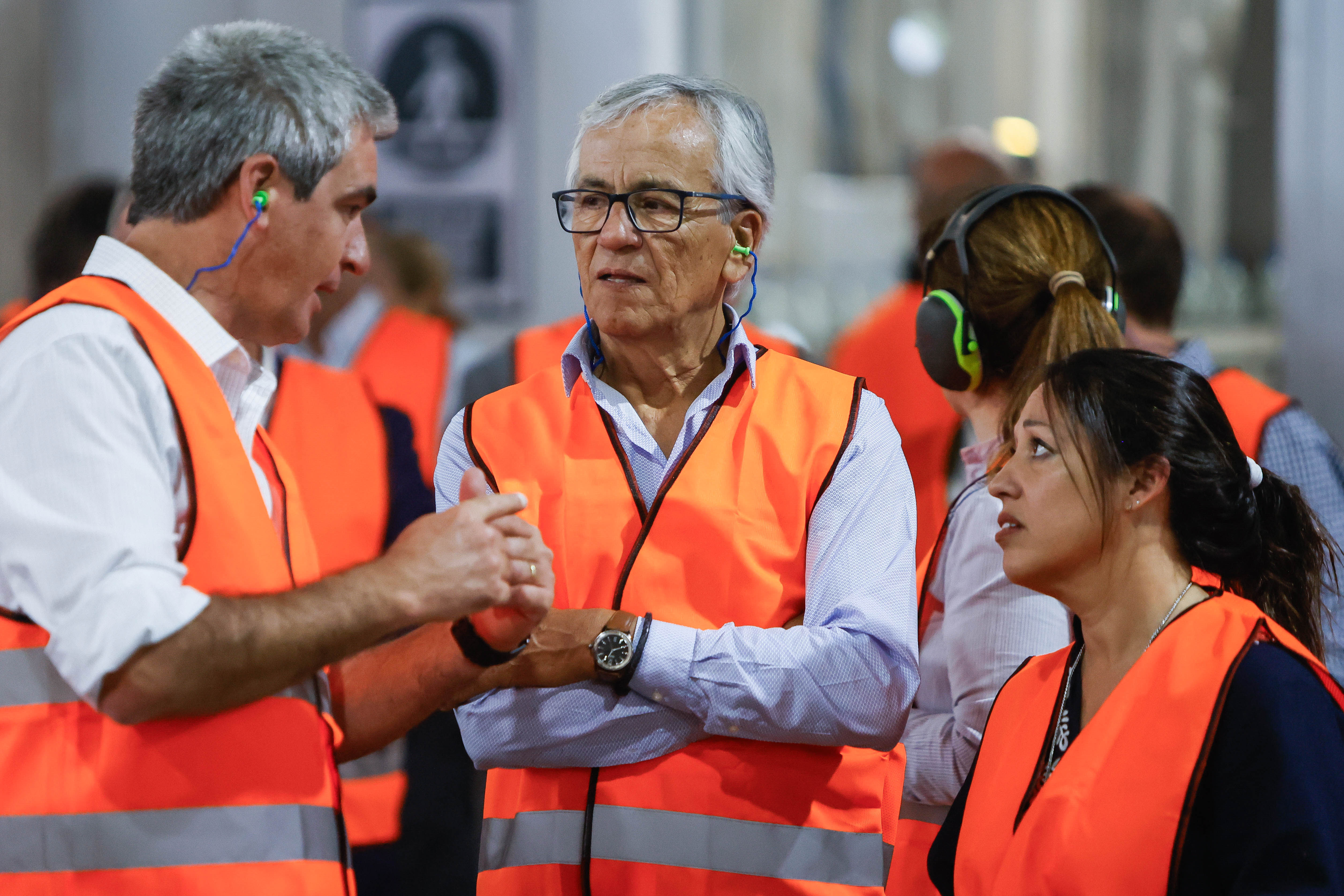 El funcionario de Salus explica el proceso a los ministros de Industria y Trabajo, quienes usan chalecos naranjas de seguridad.