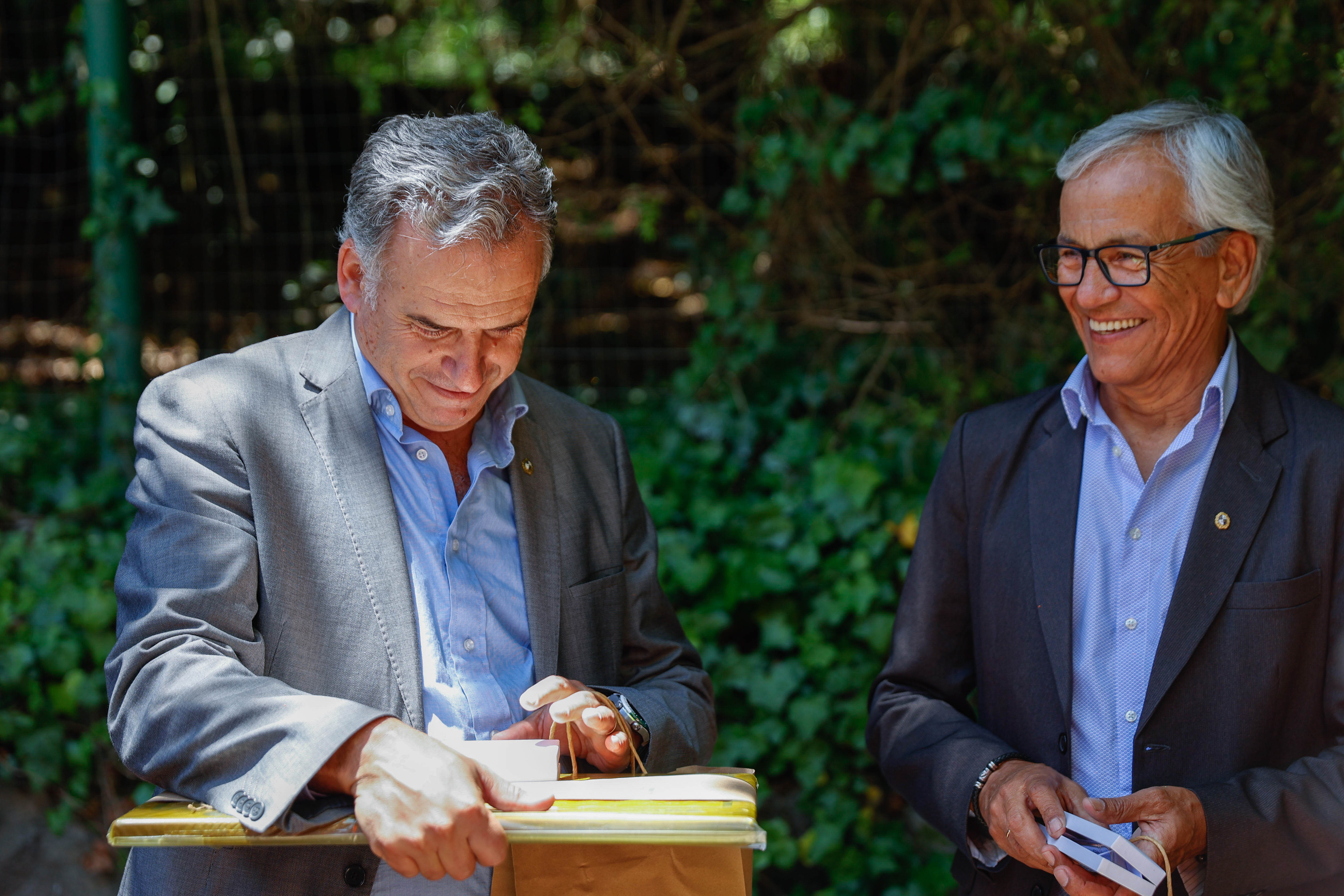 Orsi, sonriente, abre un obsequio sobre un atril, mientras el ministro de Trabajo lo observa desde atrás sonriente.