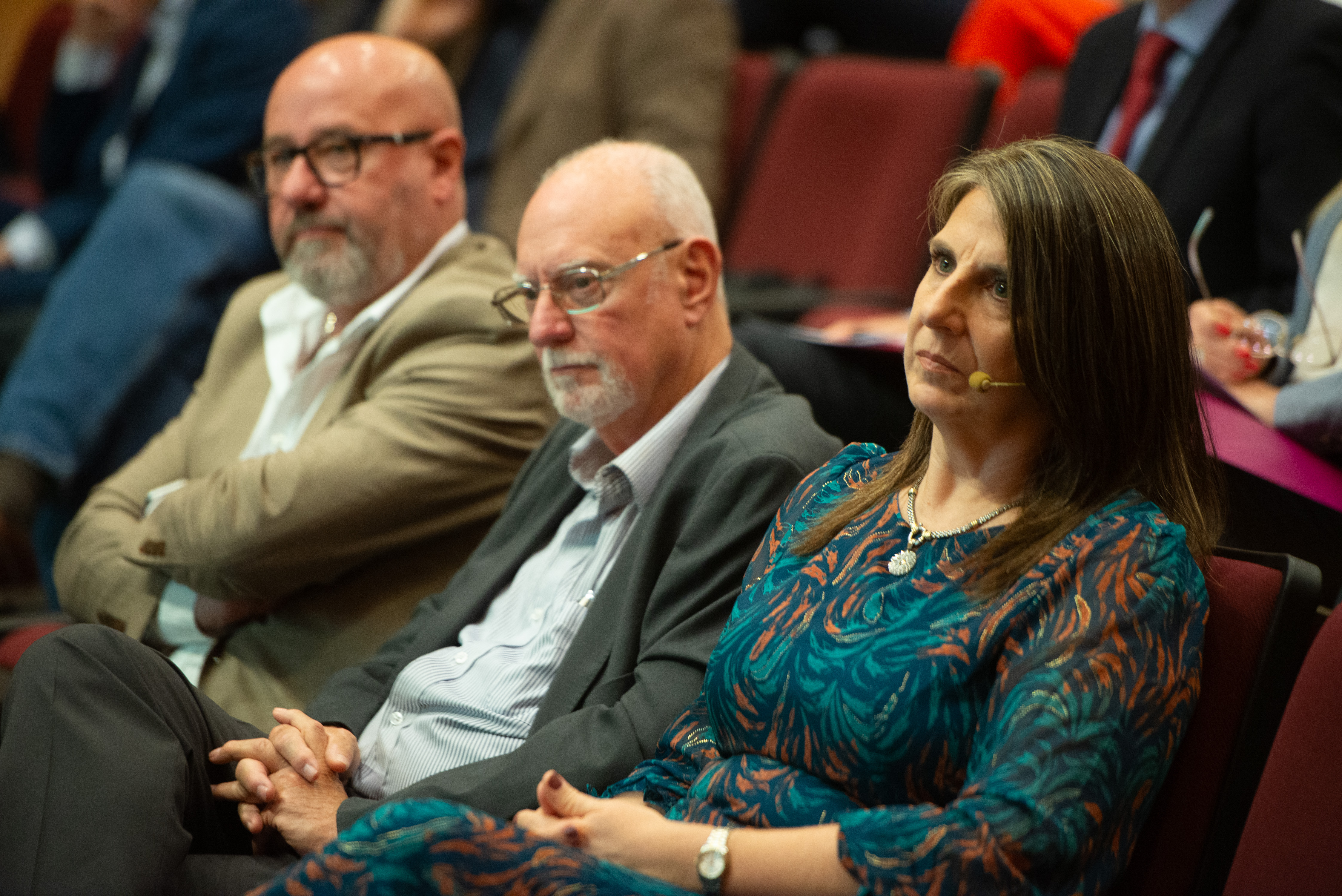 Primer plano de autoridades de Deres, sentadas en primera fila del auditorio, mirando hacia el escenario.