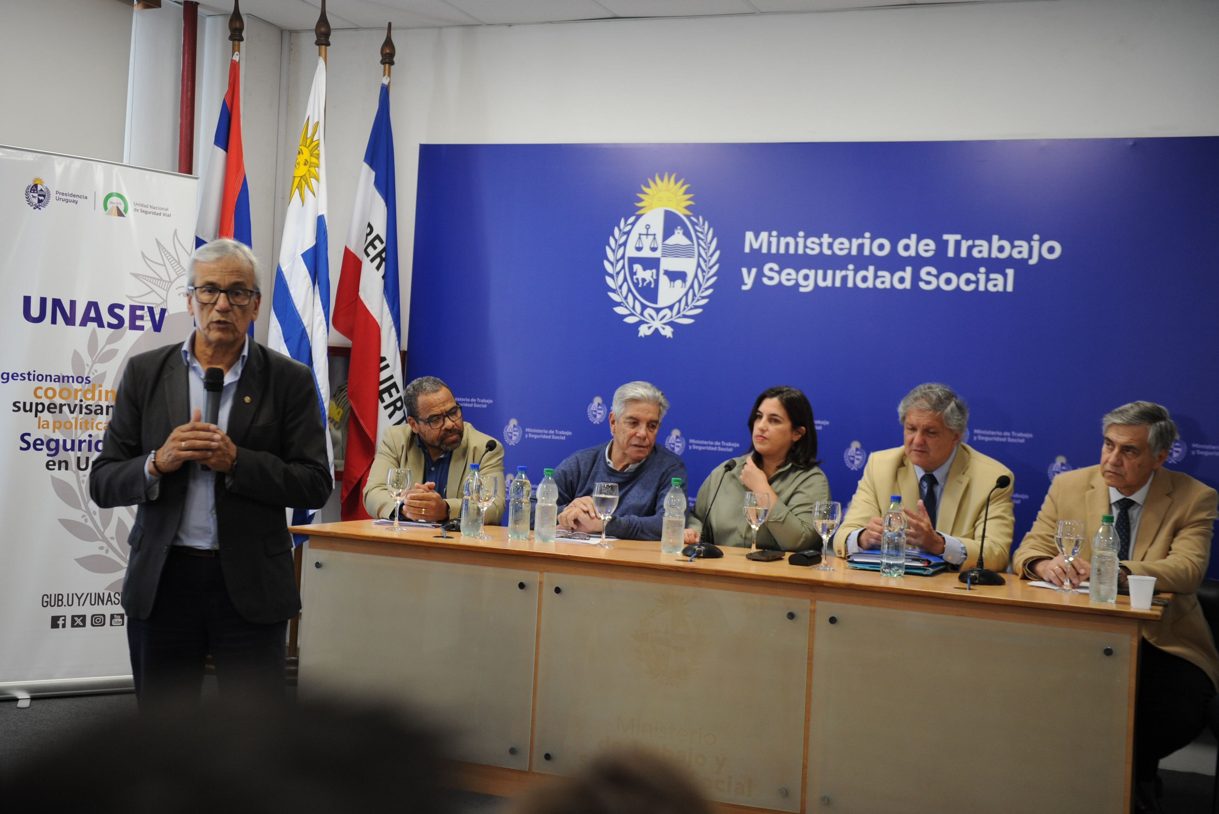 Ministro de Trabajo diserta de pie con micrófono en mano. Atrás las autoridades sentadas en mesa principal lo observan.