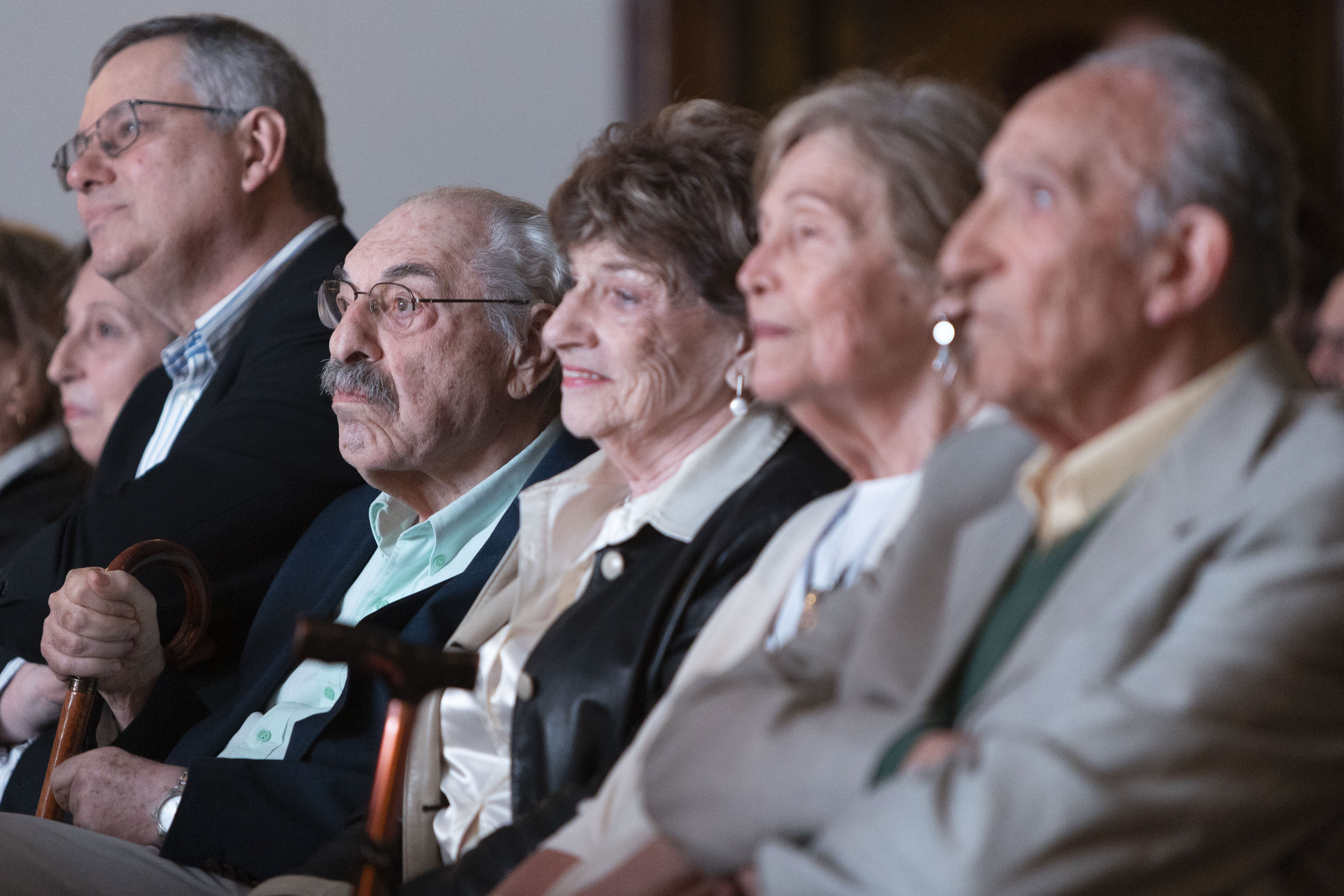 Primer plano de público sentado en la primera fila de la platea escuchando una disertación.