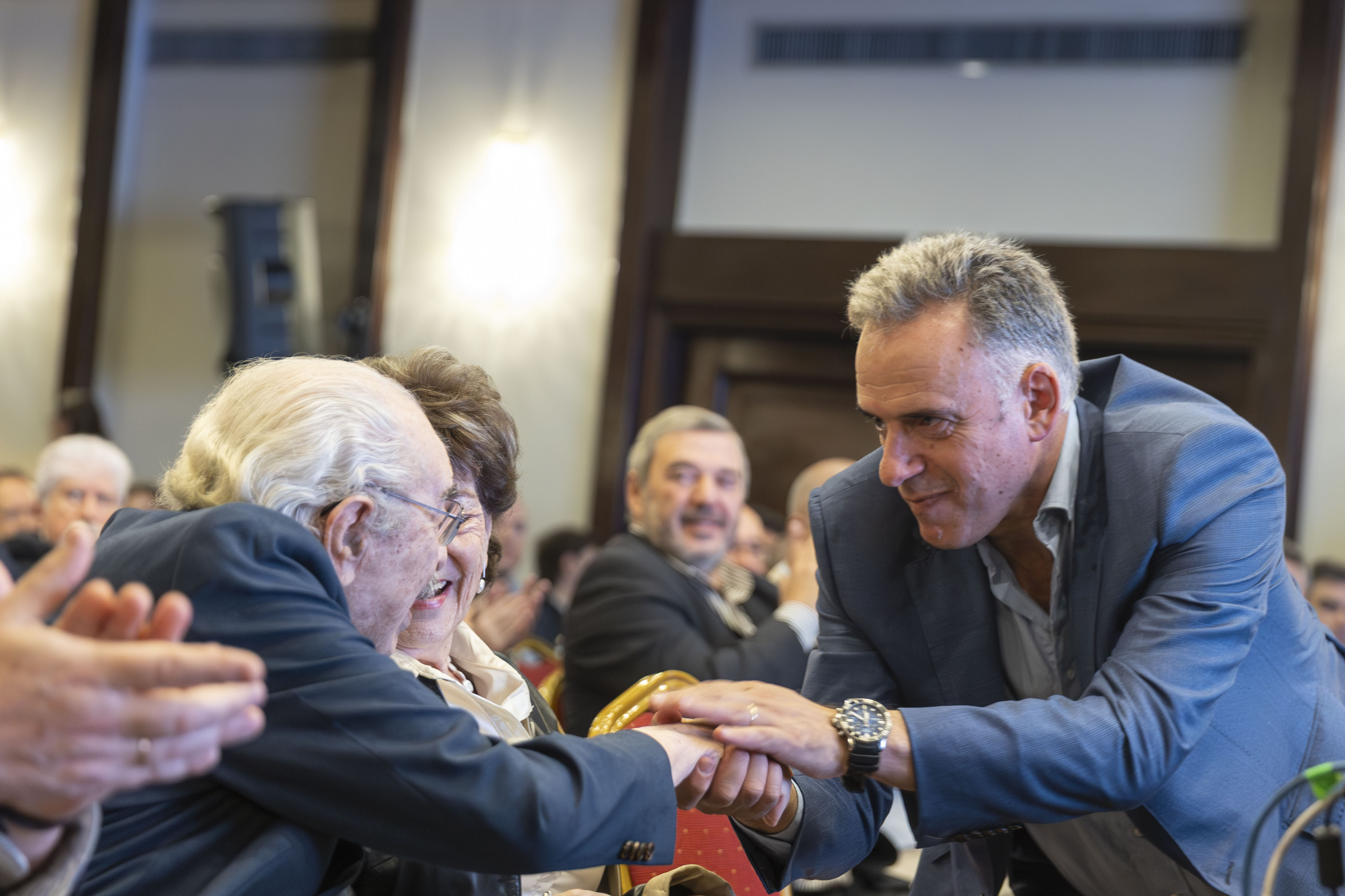 Orsi saluda afectuosamente con un apretón de manos a un asistente entre el público.