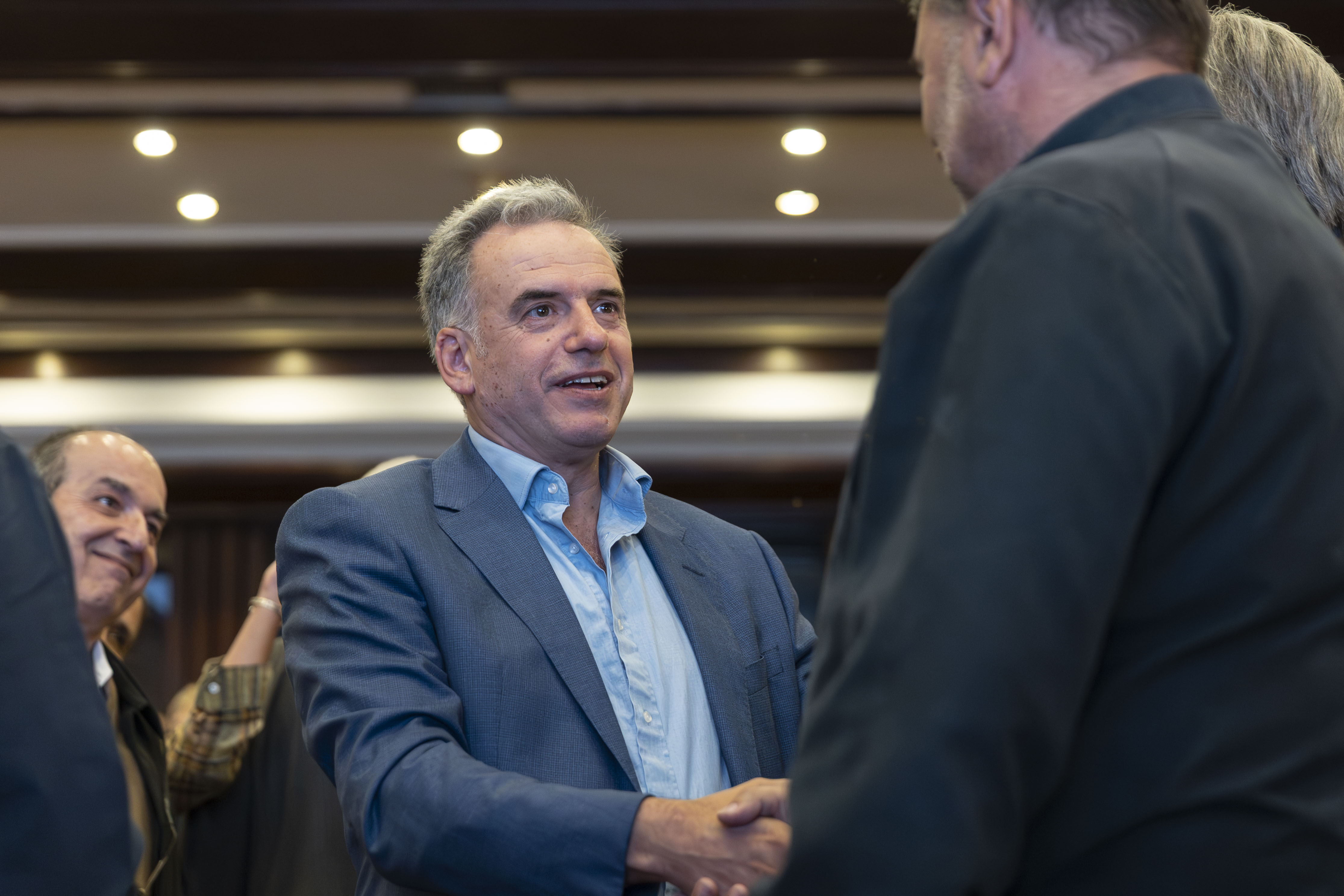 Orsi, de pie, estrecha la mano de un asistente en la sala de ingreso al evento.