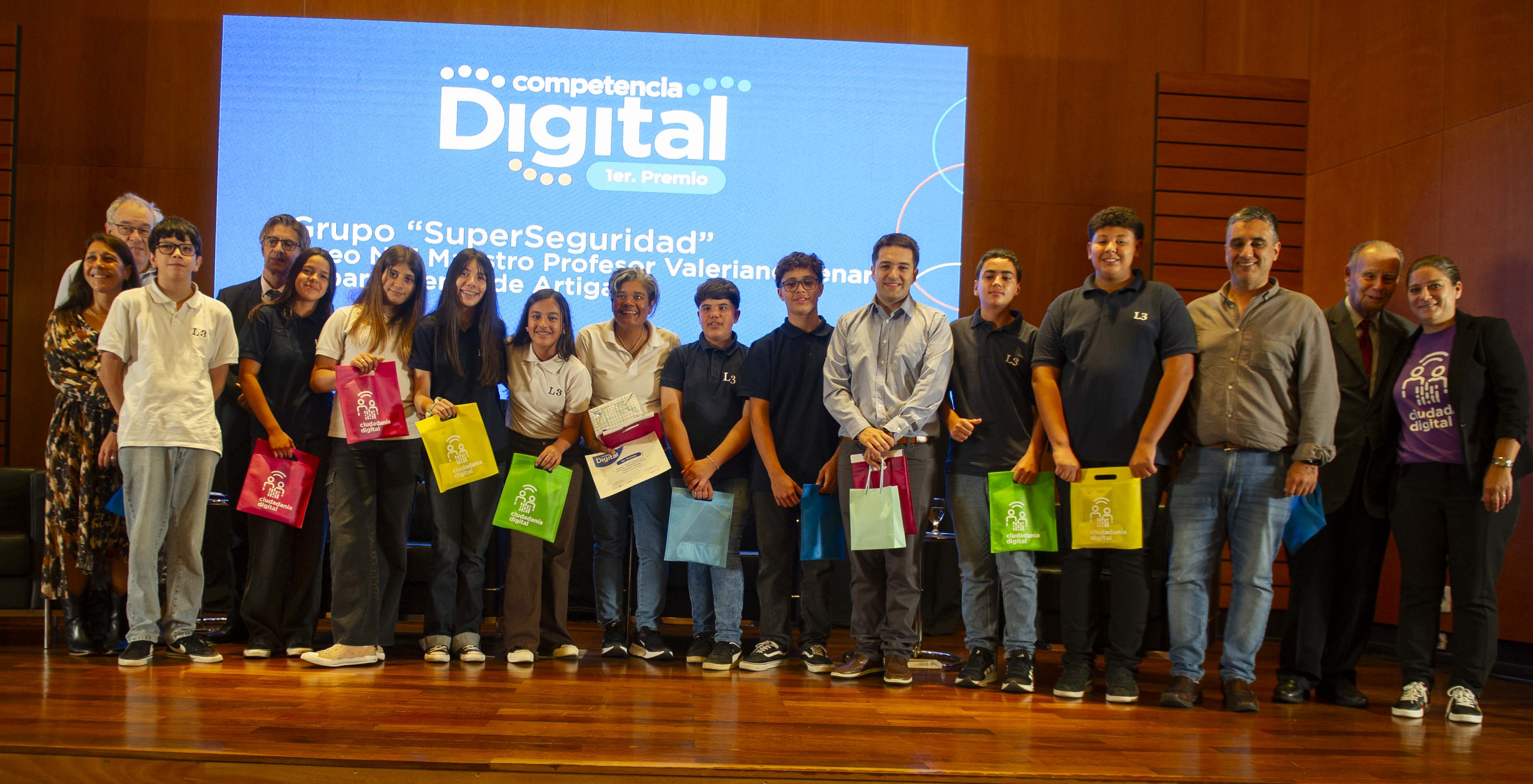 Estudiantes y docentes del liceo n.° 3 de Artigas y autoridades de Agesic posan sonrientes frente a cámara en escenario del auditorio de Presidencia.