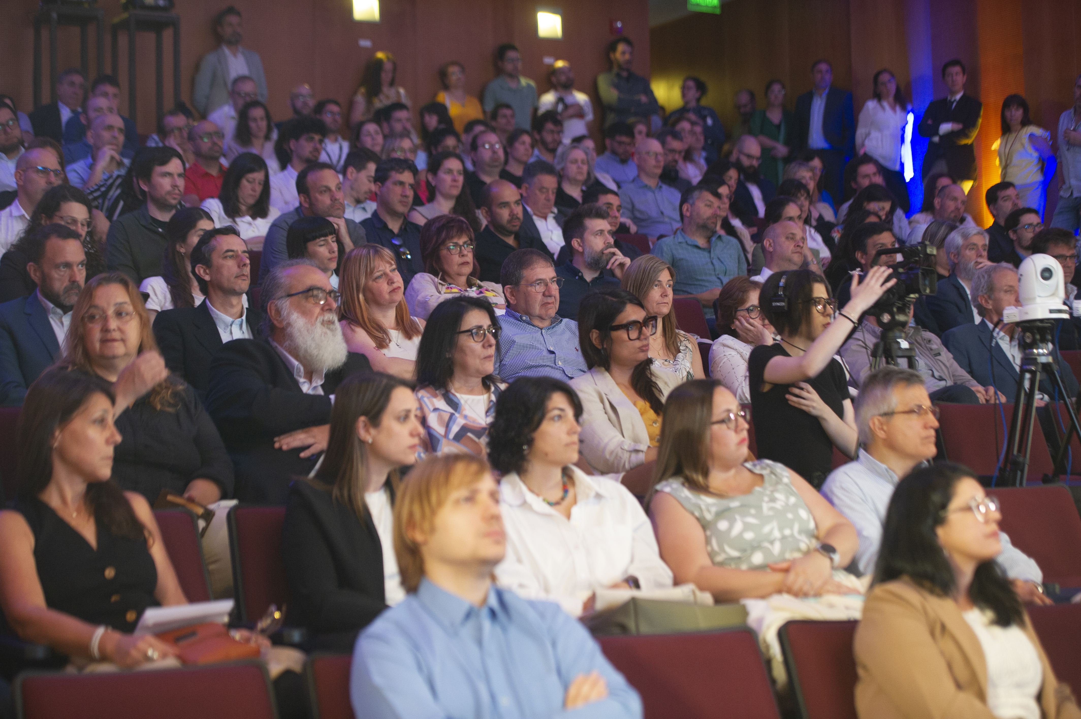Plano general del público sentado en la platea del auditorio escuchando una disertación.