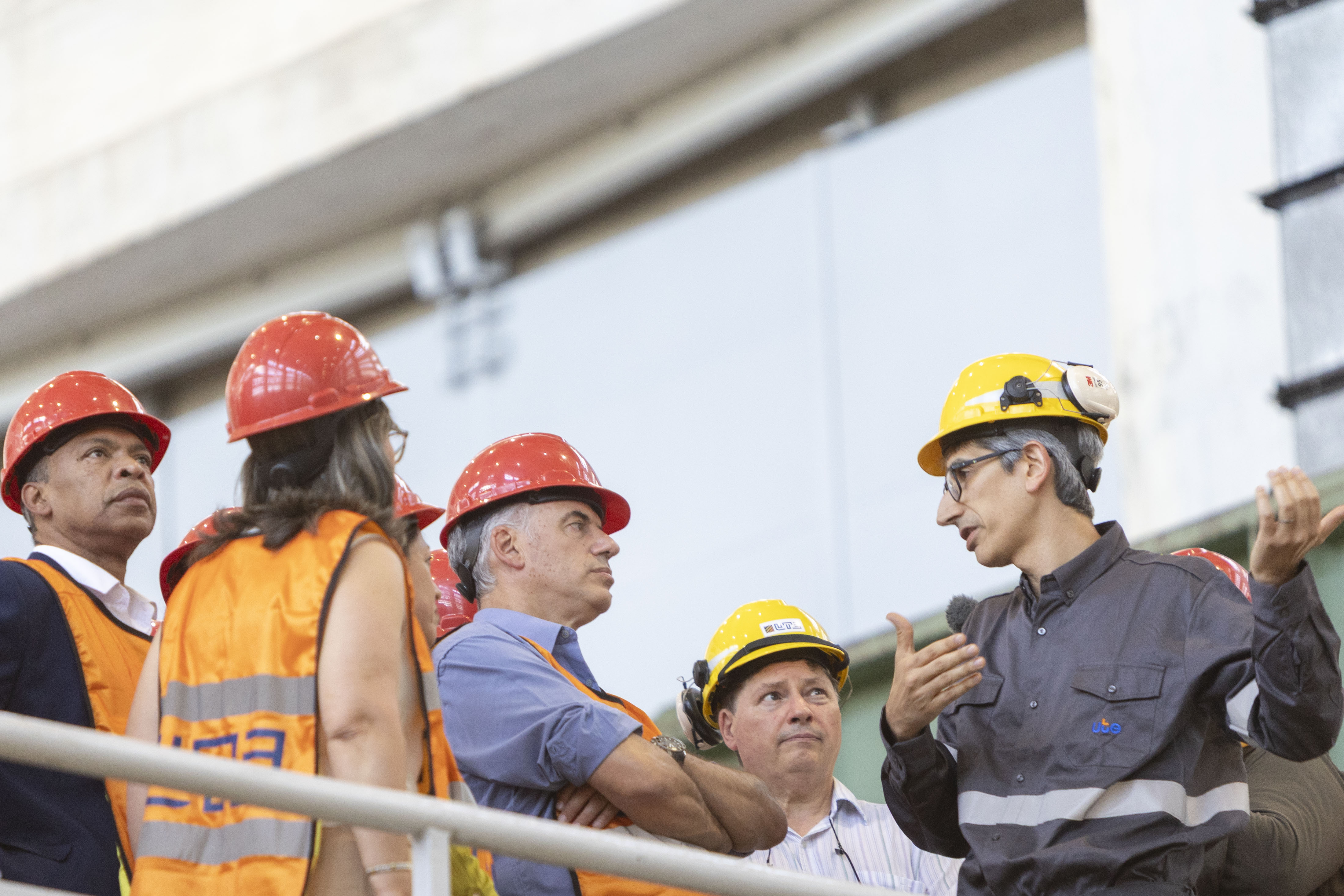 Orsi junto a un grupo de personas con cascos rojos y amarillos y chalecos naranjas escucha una explicación en la central hidroeléctrica.