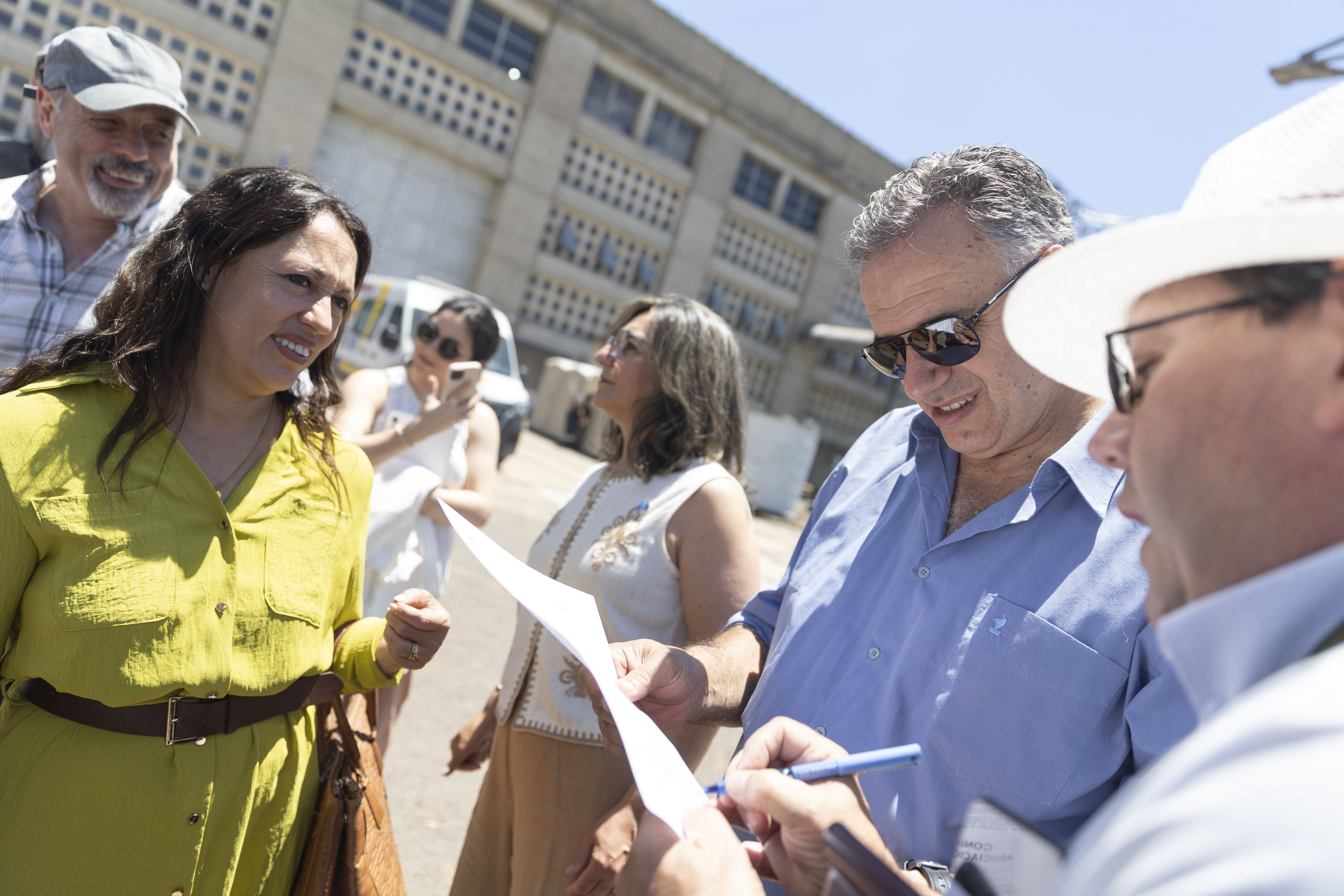 Primer plano de Orsi mirando unos papeles y conversando con otras personas al aire libre.