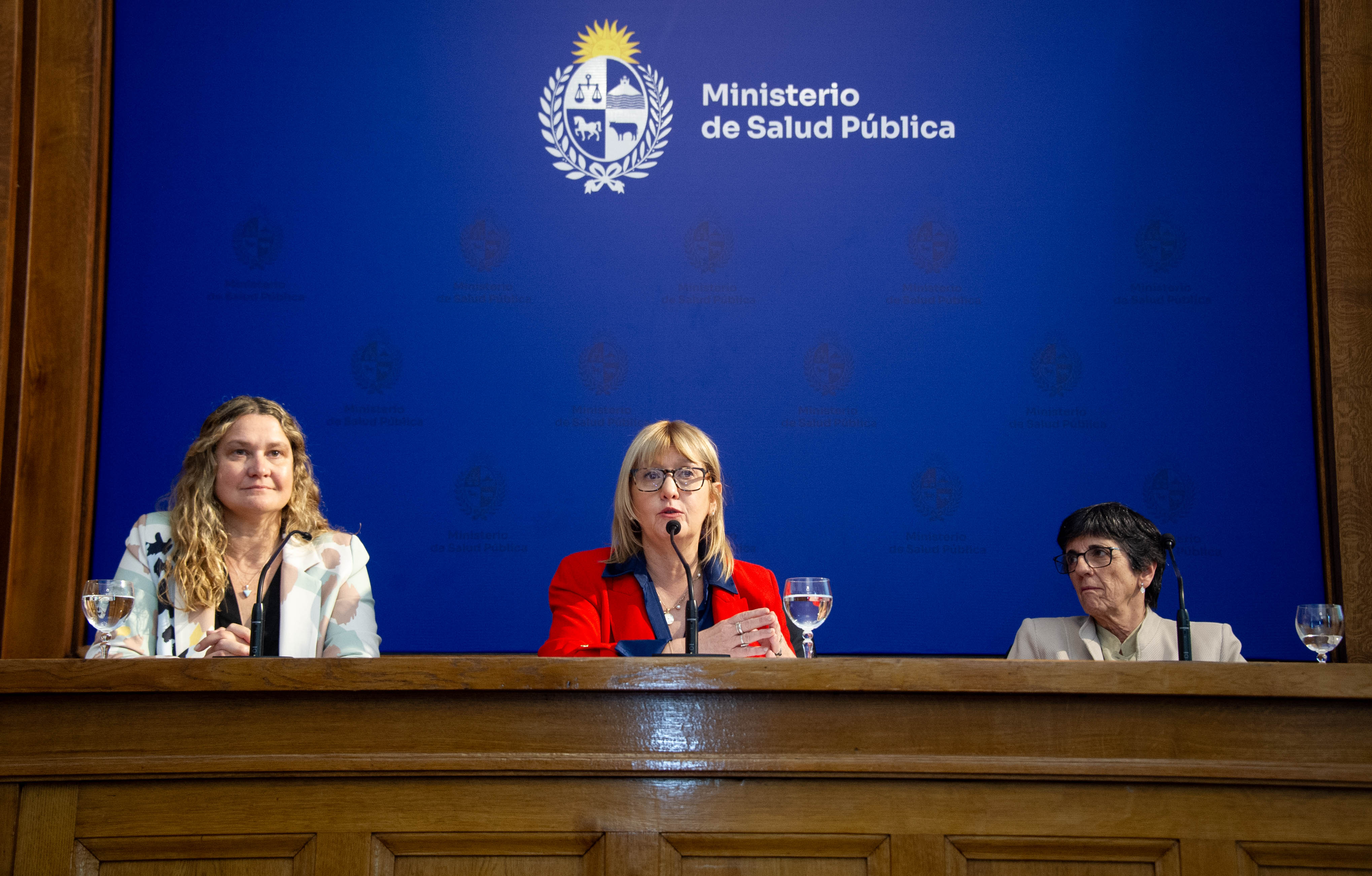 Ministra de Salud Pública diserta sentada en mesa con micrófono junto a la presidenta y la directora del Fondo Nacional de Recursos.