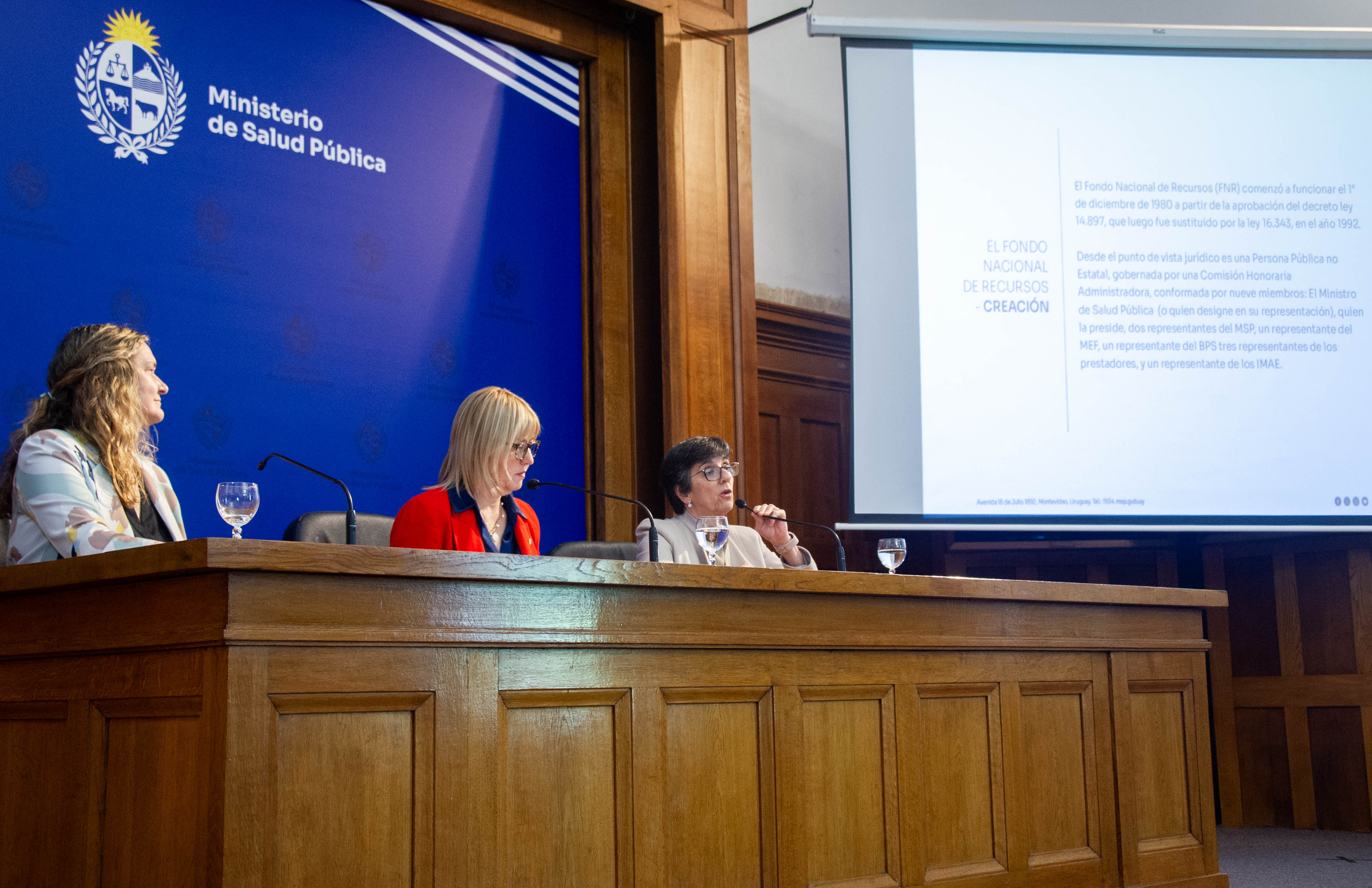 Plano general de la mesa principal con las autoridades prontas para disertar. Al costado hay una pantalla donde se proyecta una presentación.